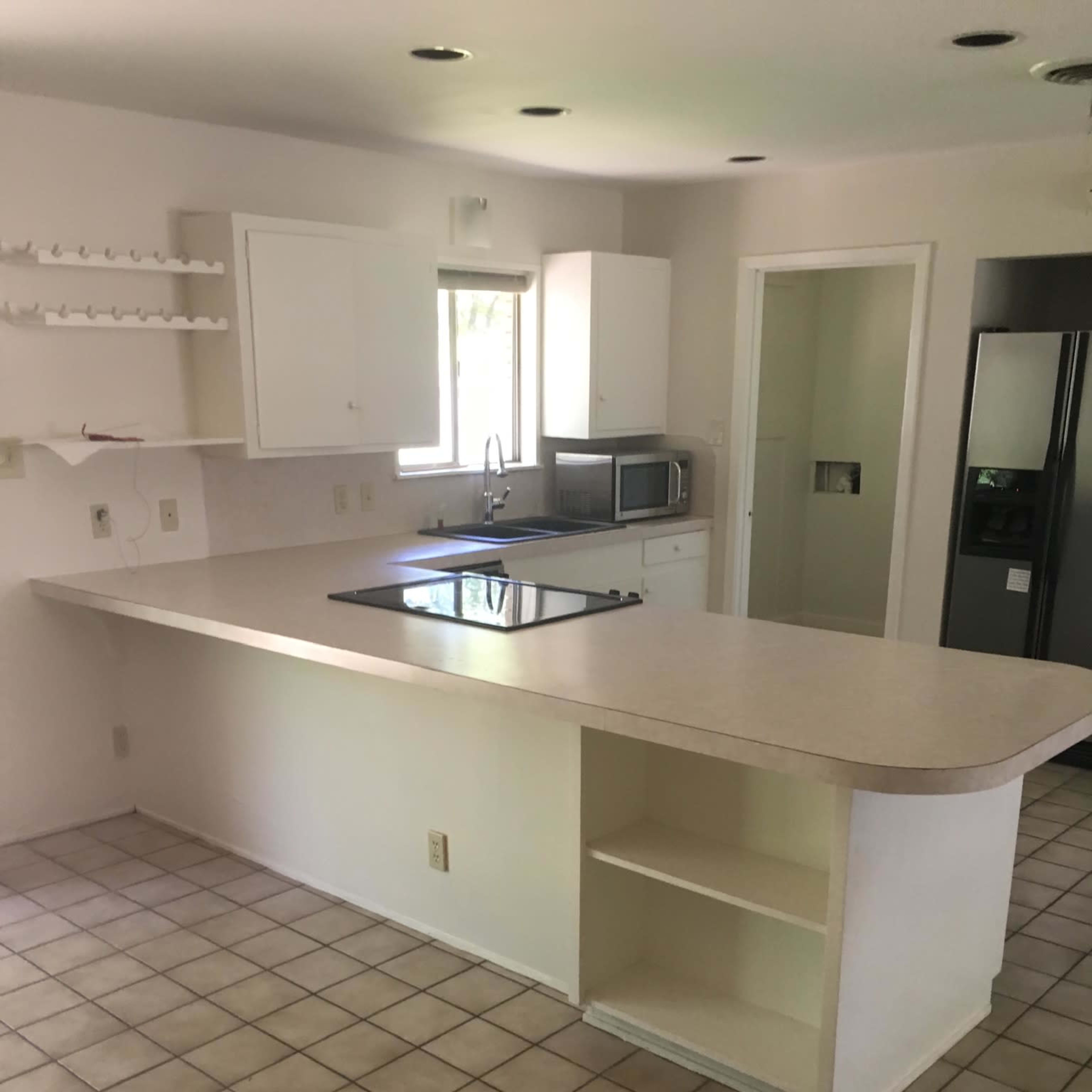 A kitchen with a tile floor, an island with a cooktop, and white cabinetry, is visible, featuring a microwave and refrigerator.