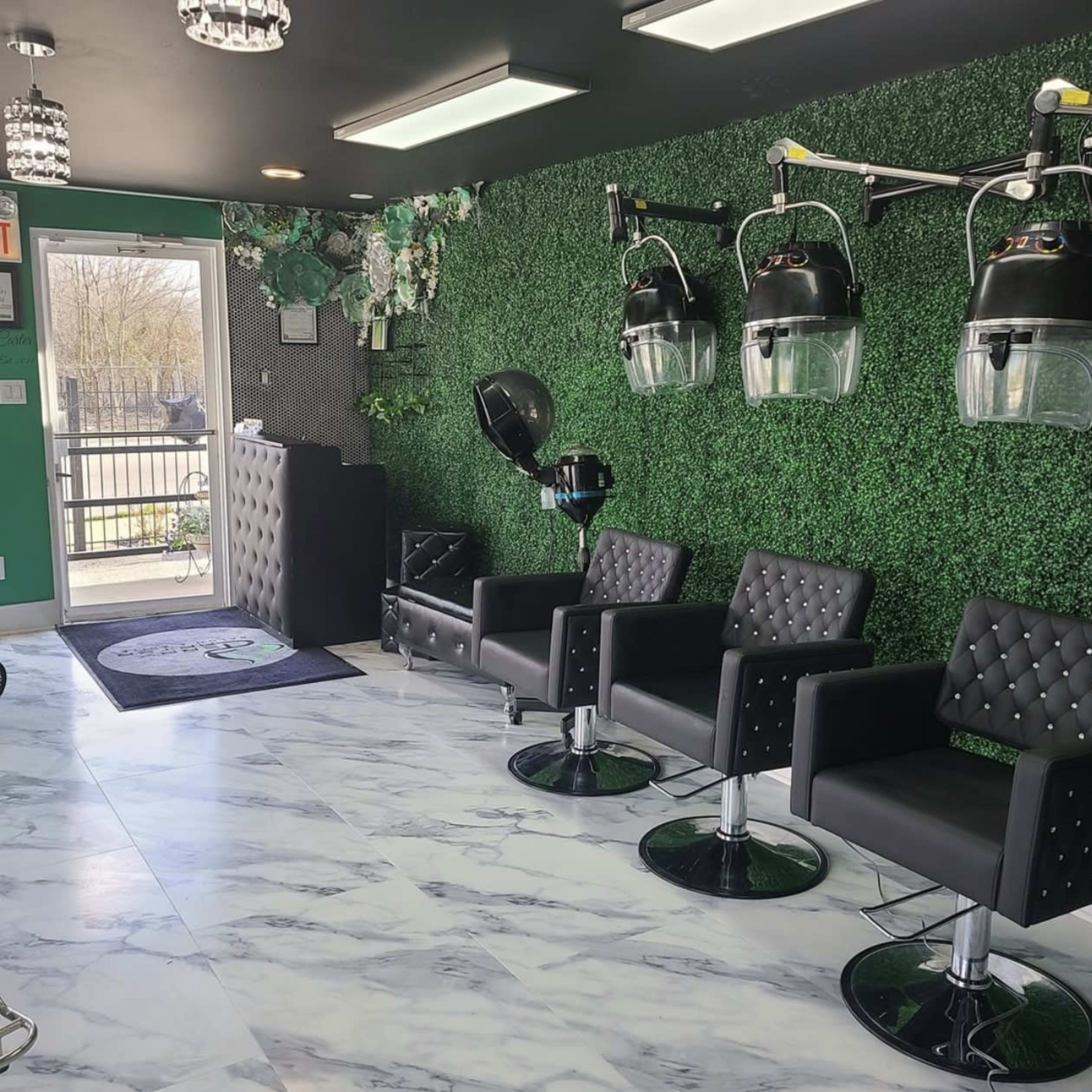 A modern salon interior with black leather chairs, a green plant wall, and hooded hair dryers on stands.