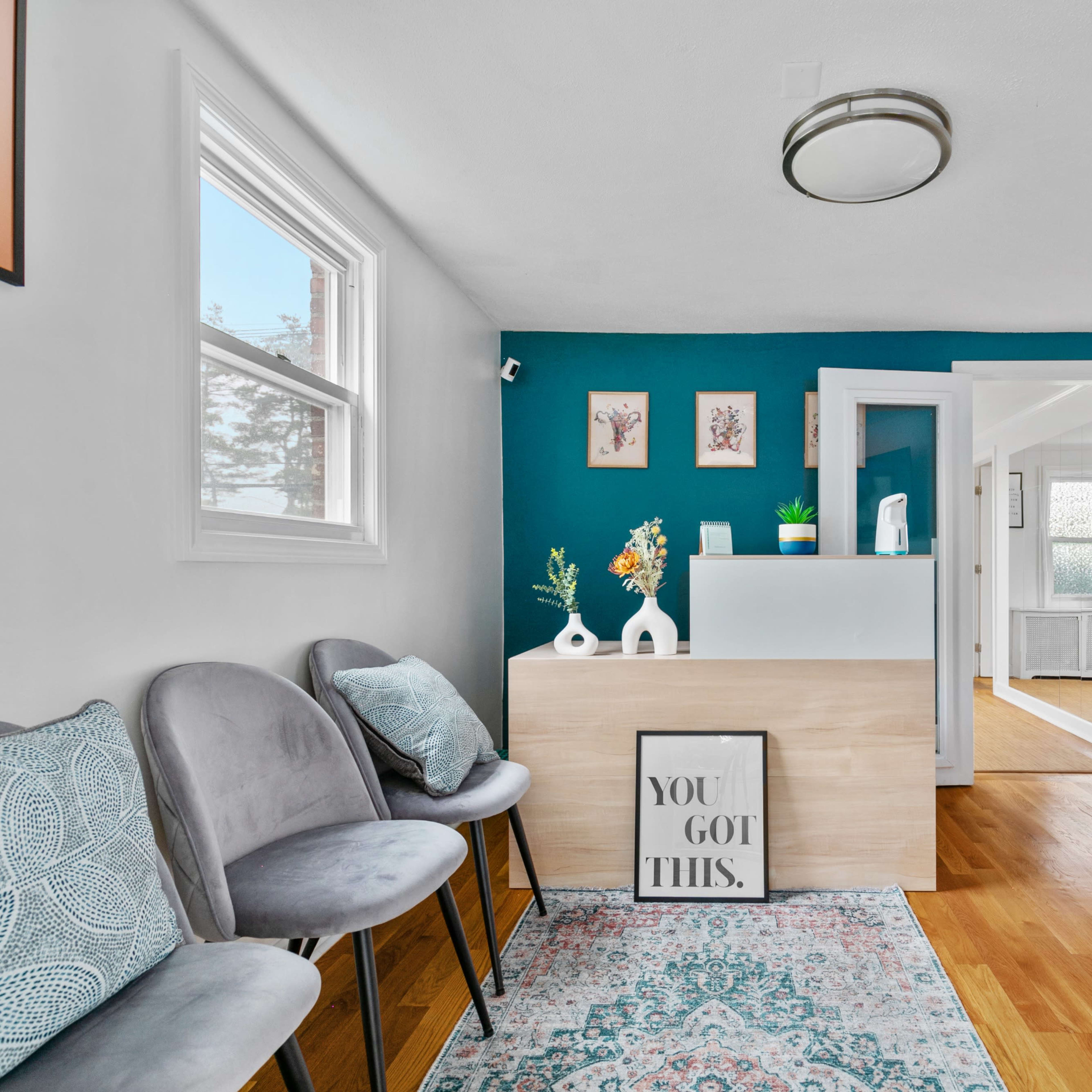A bright reception area featuring a wooden front desk, gray chairs, and teal accent walls adorned with framed artwork.
