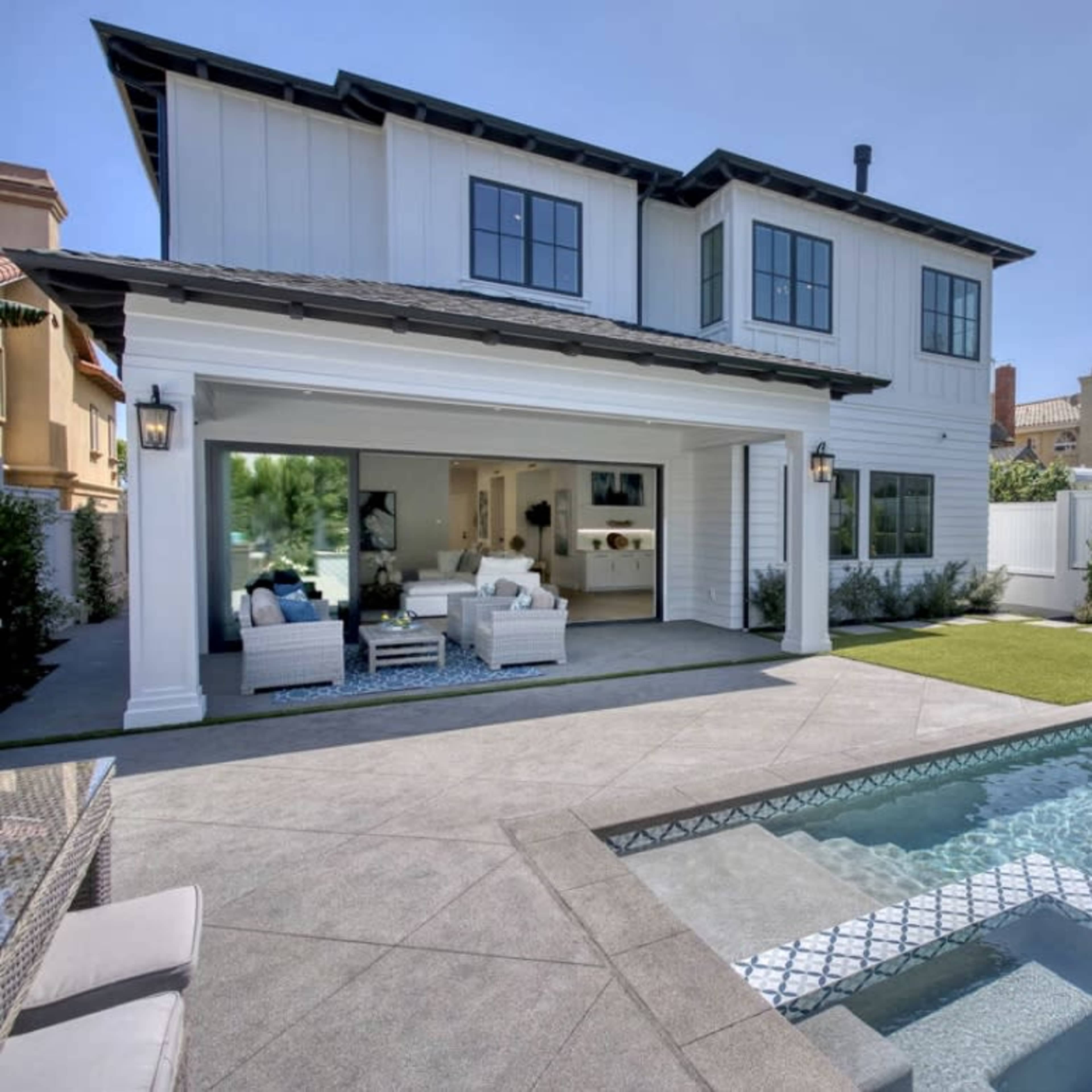 A modern two-story house with a pool and outdoor seating area in a residential backyard.