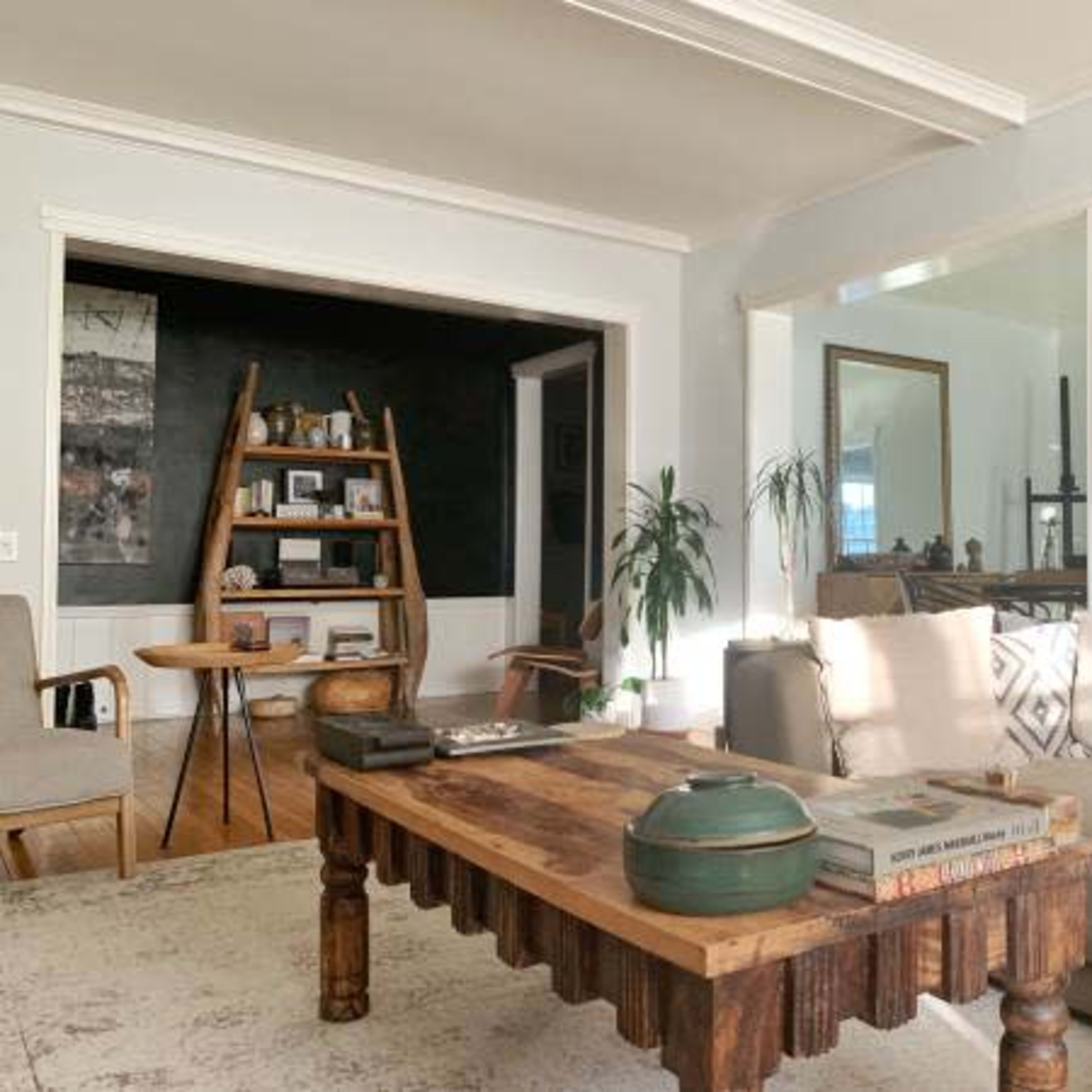 A modern living room features a large wooden coffee table, a sectional sofa, and a wall with dark paint, along with decorative items and artwork.