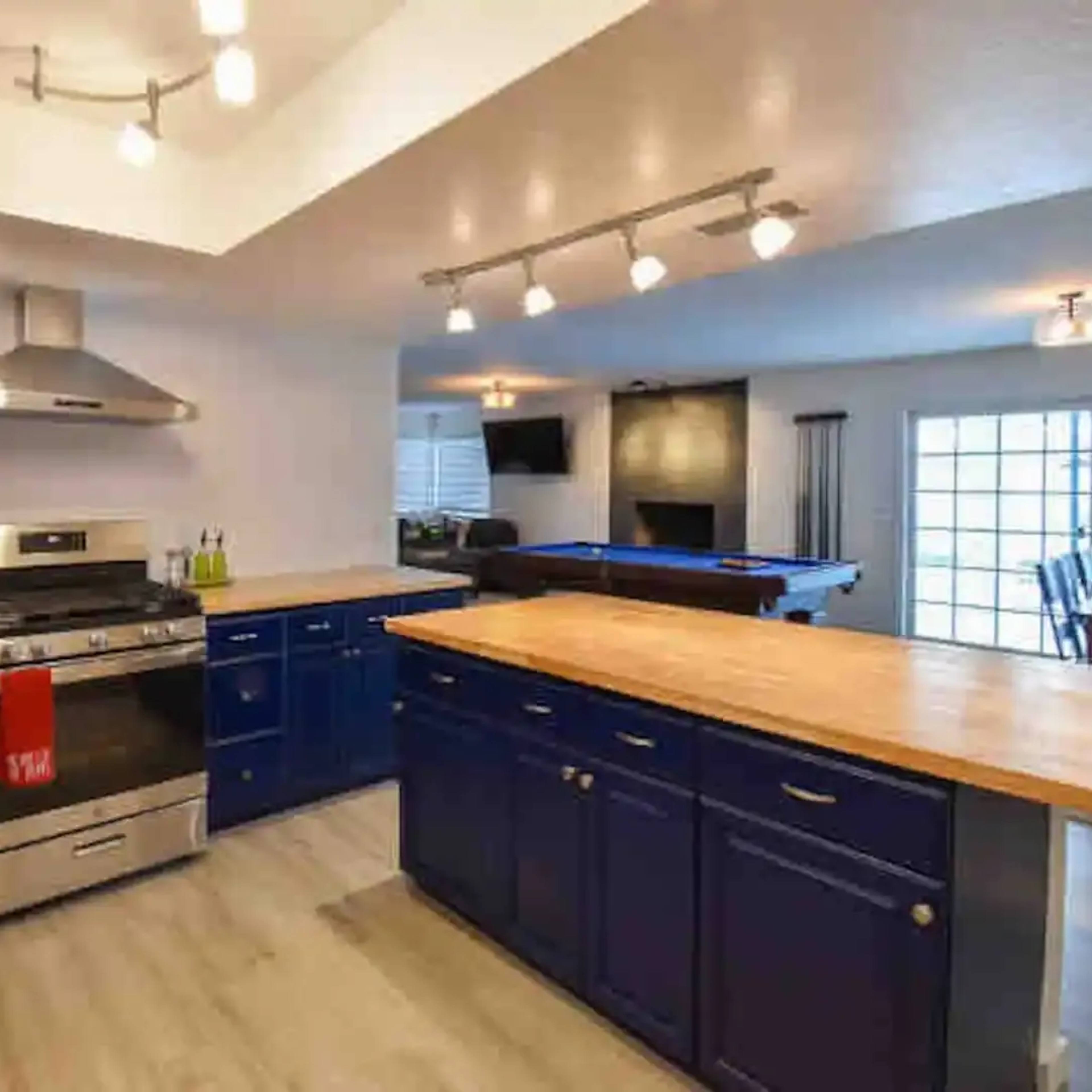 The kitchen features blue cabinets with wooden countertops, a stainless steel gas stove, and modern lighting fixtures.