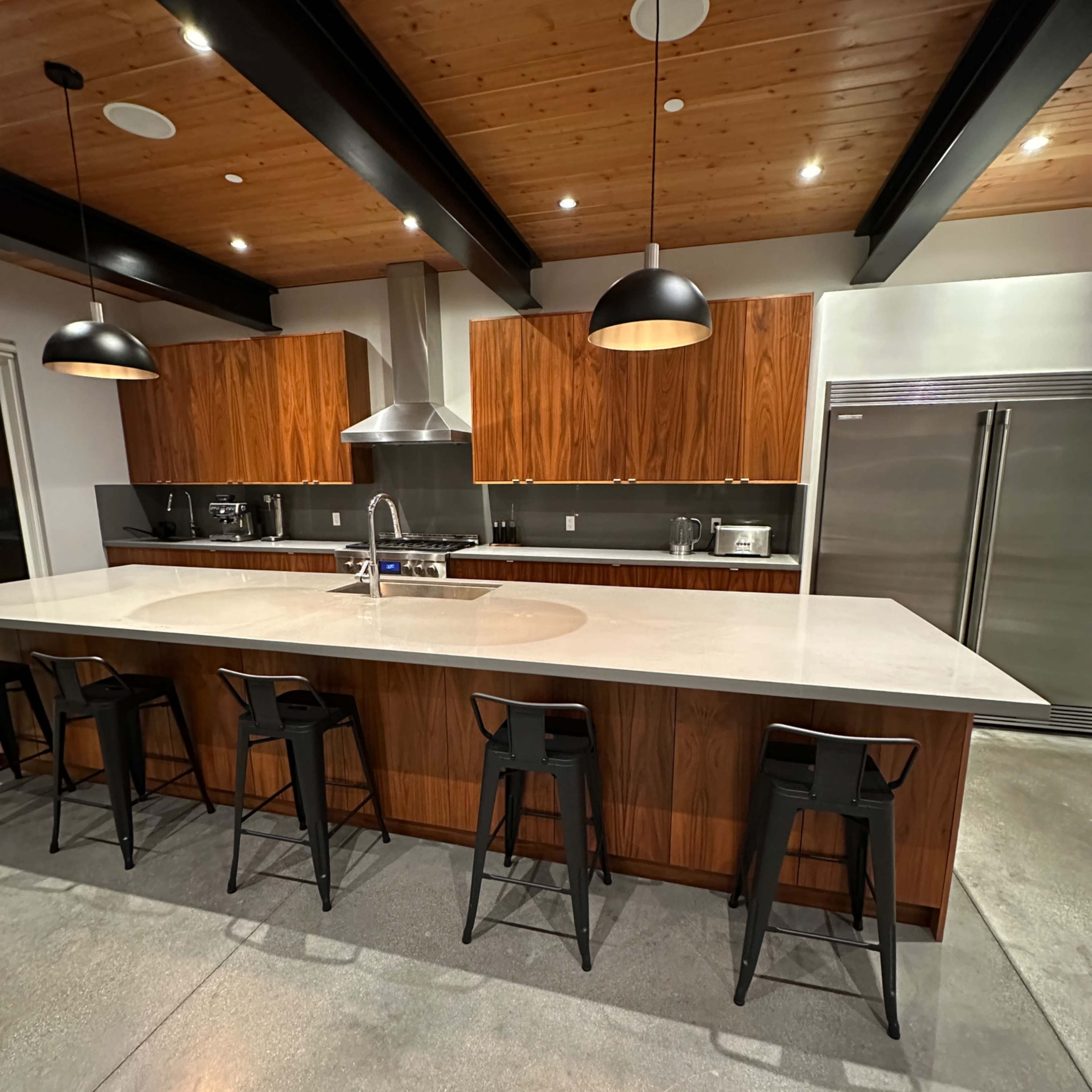 A modern kitchen with a large island, wooden cabinets, stainless steel appliances, and pendant lighting.