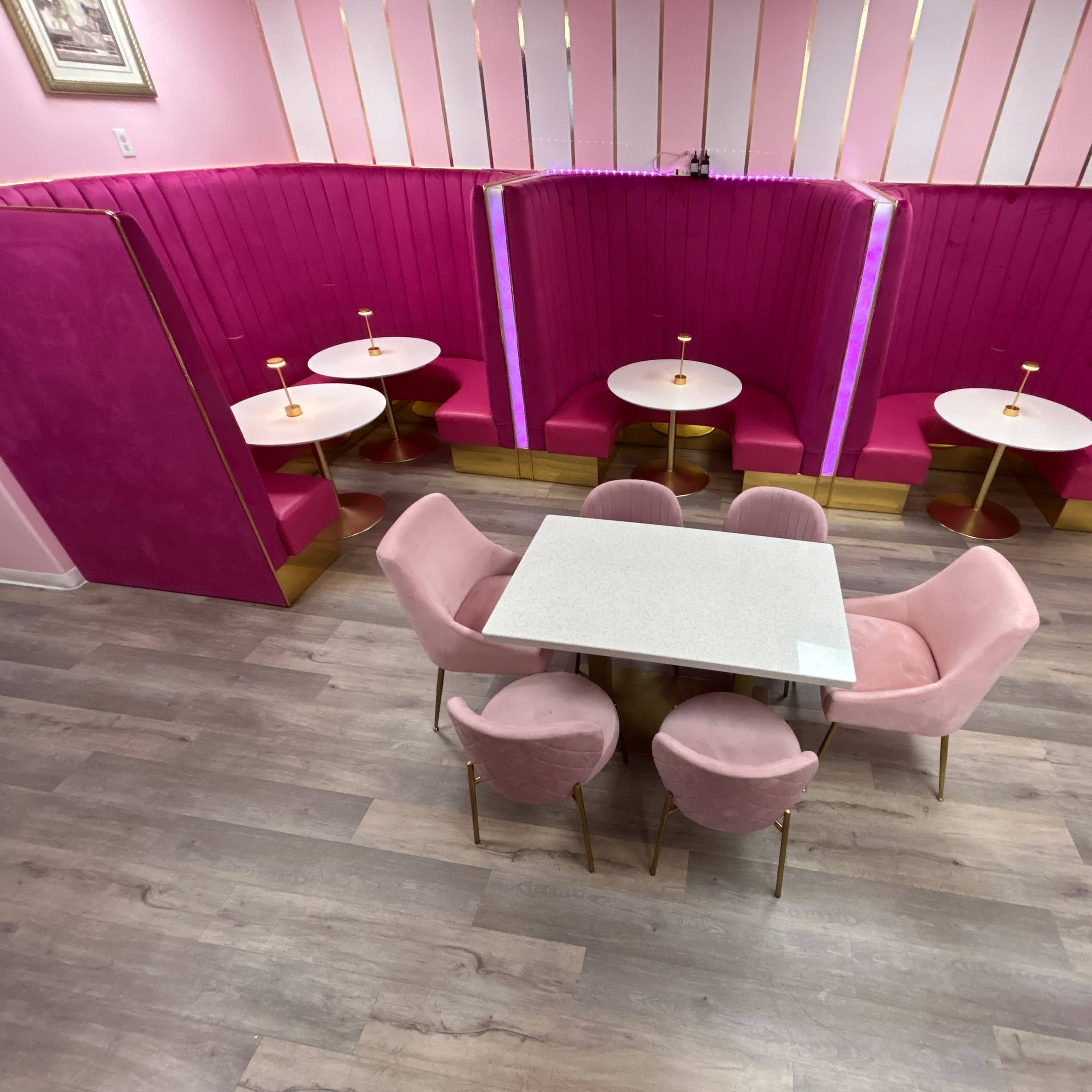 A café interior featuring pink walls and seating with a combination of tables and plush chairs arranged in a cozy layout.