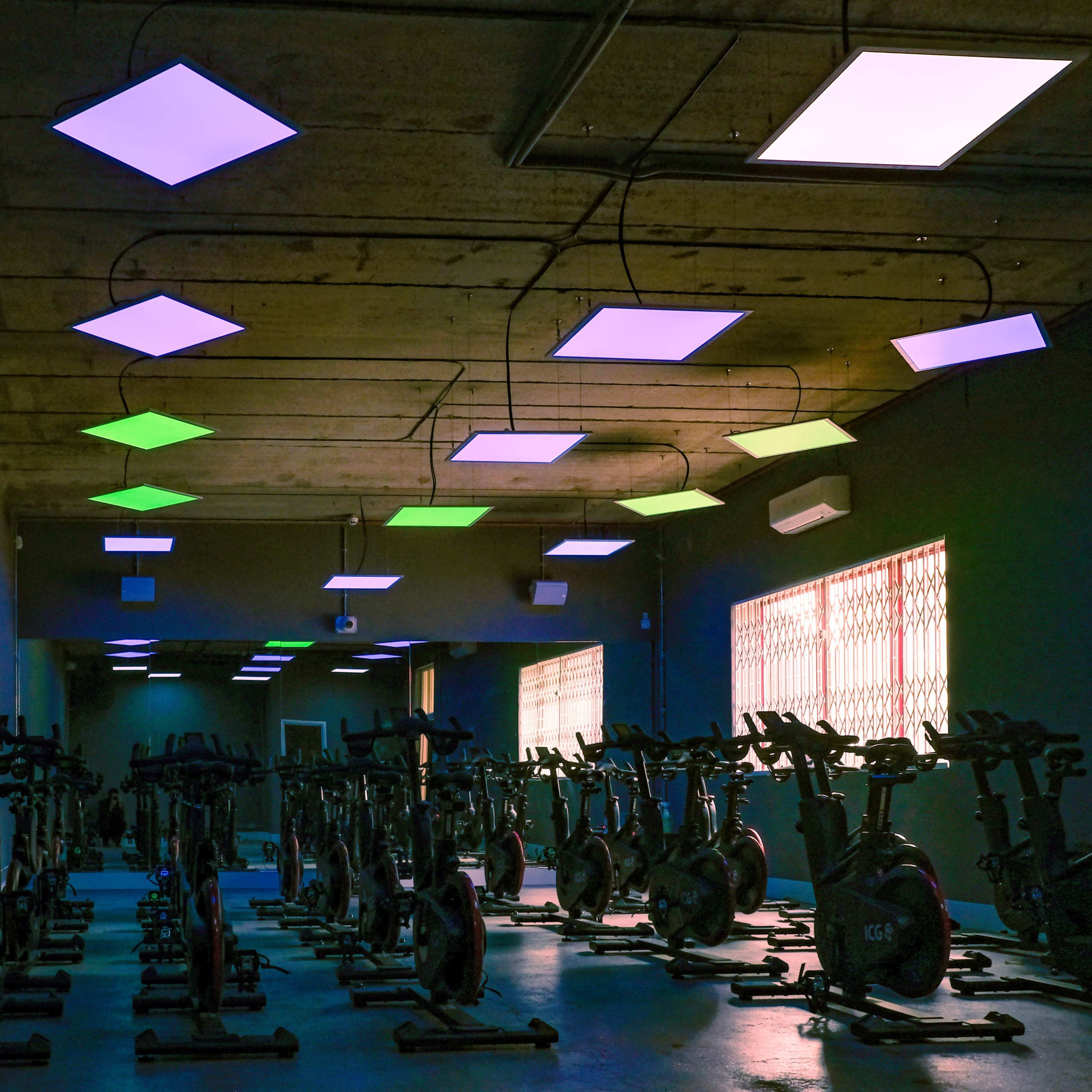 A dimly lit indoor cycling studio with multiple stationary bikes arranged in rows beneath colorful ceiling lights.