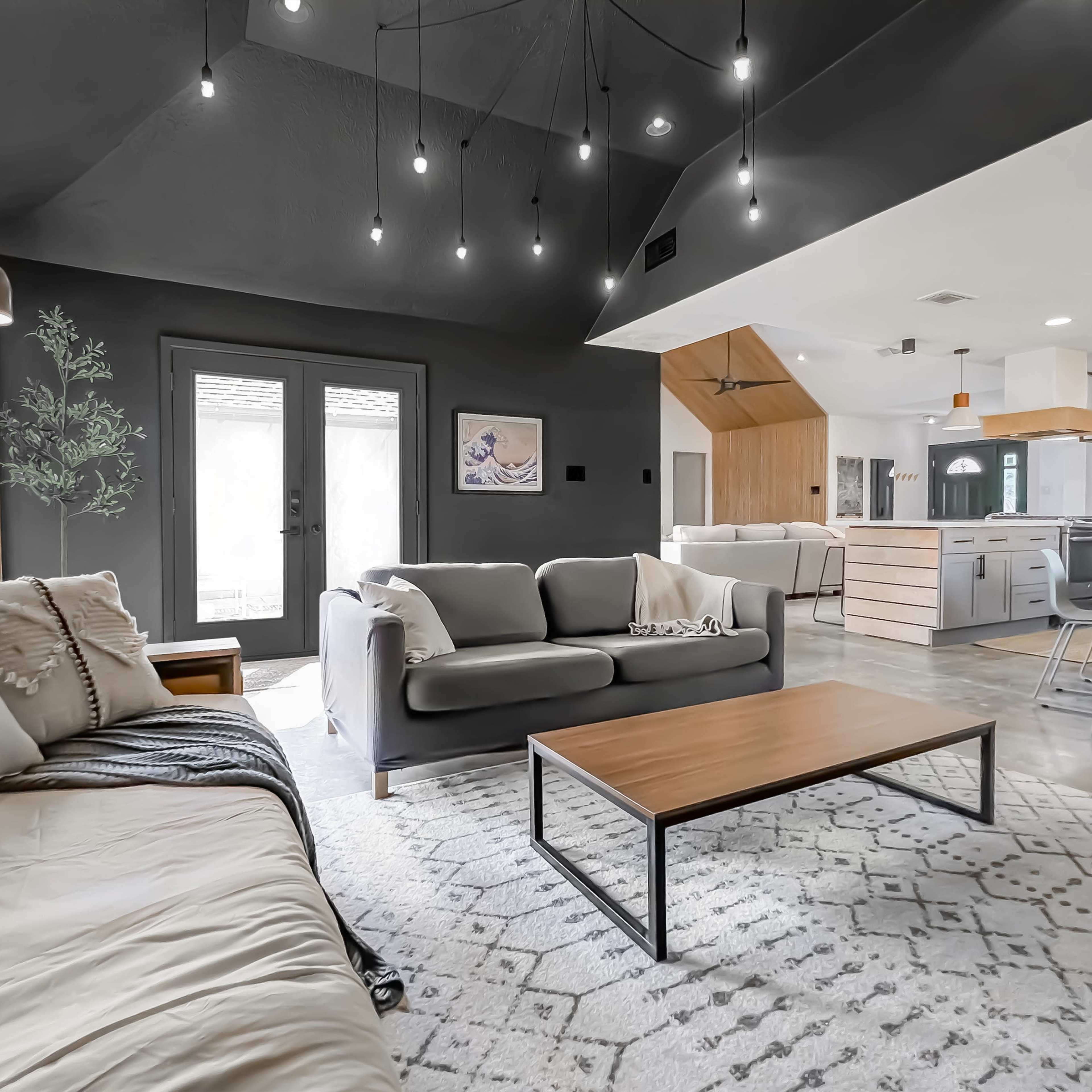 A modern living room featuring a light gray sofa, a wooden coffee table, and large windows with a view of a patio.