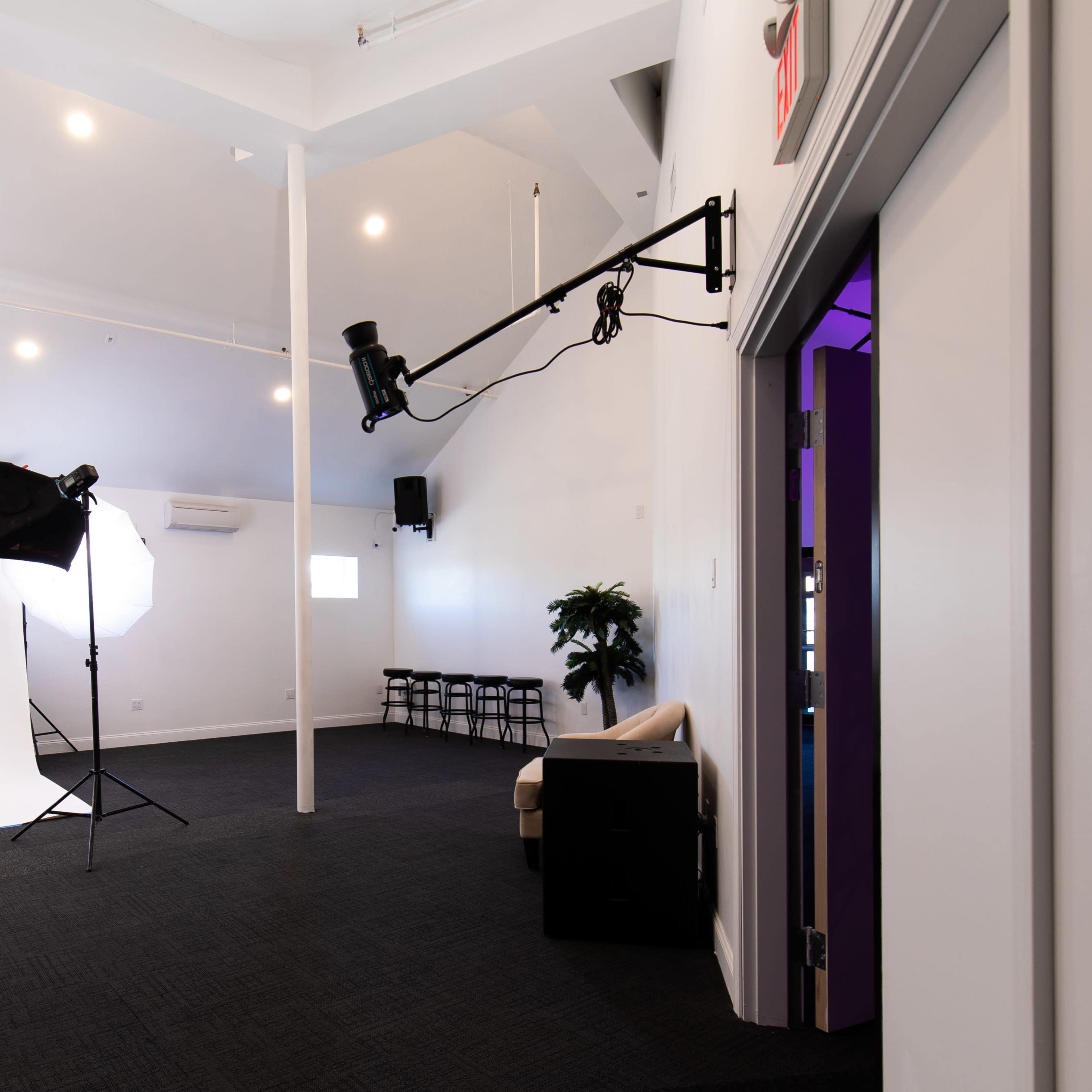 A photography studio with a white backdrop, a stool, softbox lighting, and a small seating area.