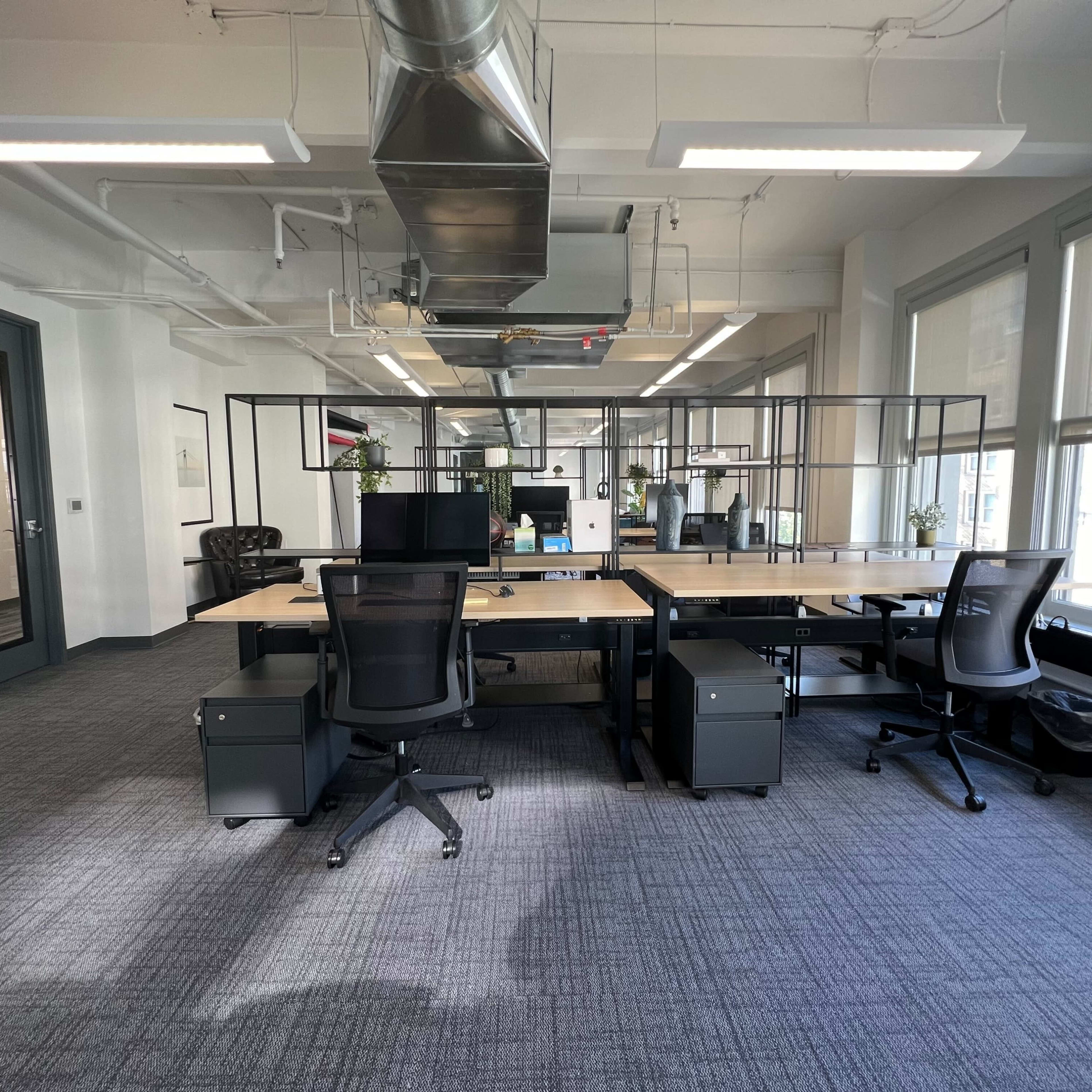 A modern office space with two desks facing each other, surrounded by glass partitions and equipped with ergonomic chairs and computer monitors.