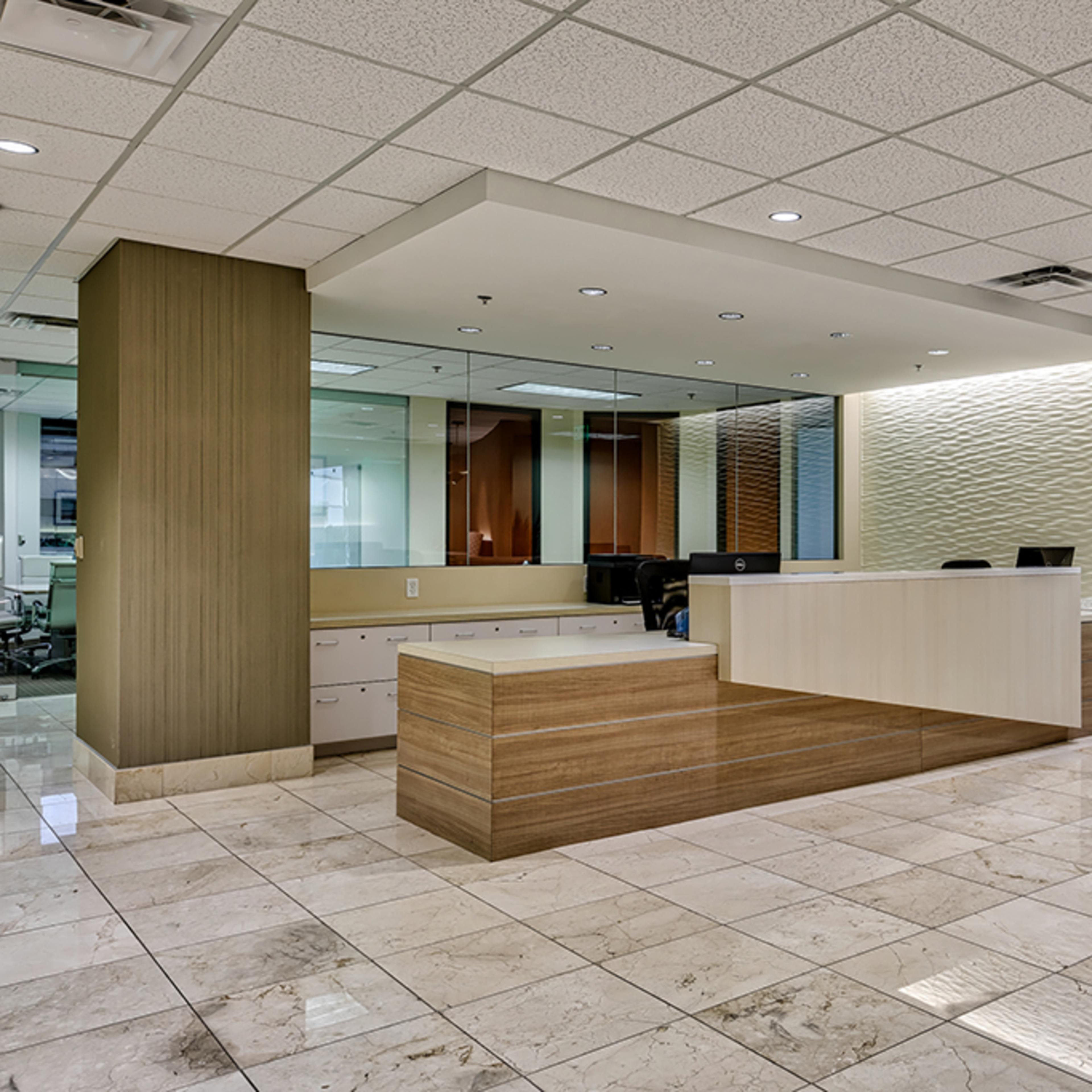 A modern office reception area with a wooden front desk, polished marble flooring, and a softly lit wall backdrop.