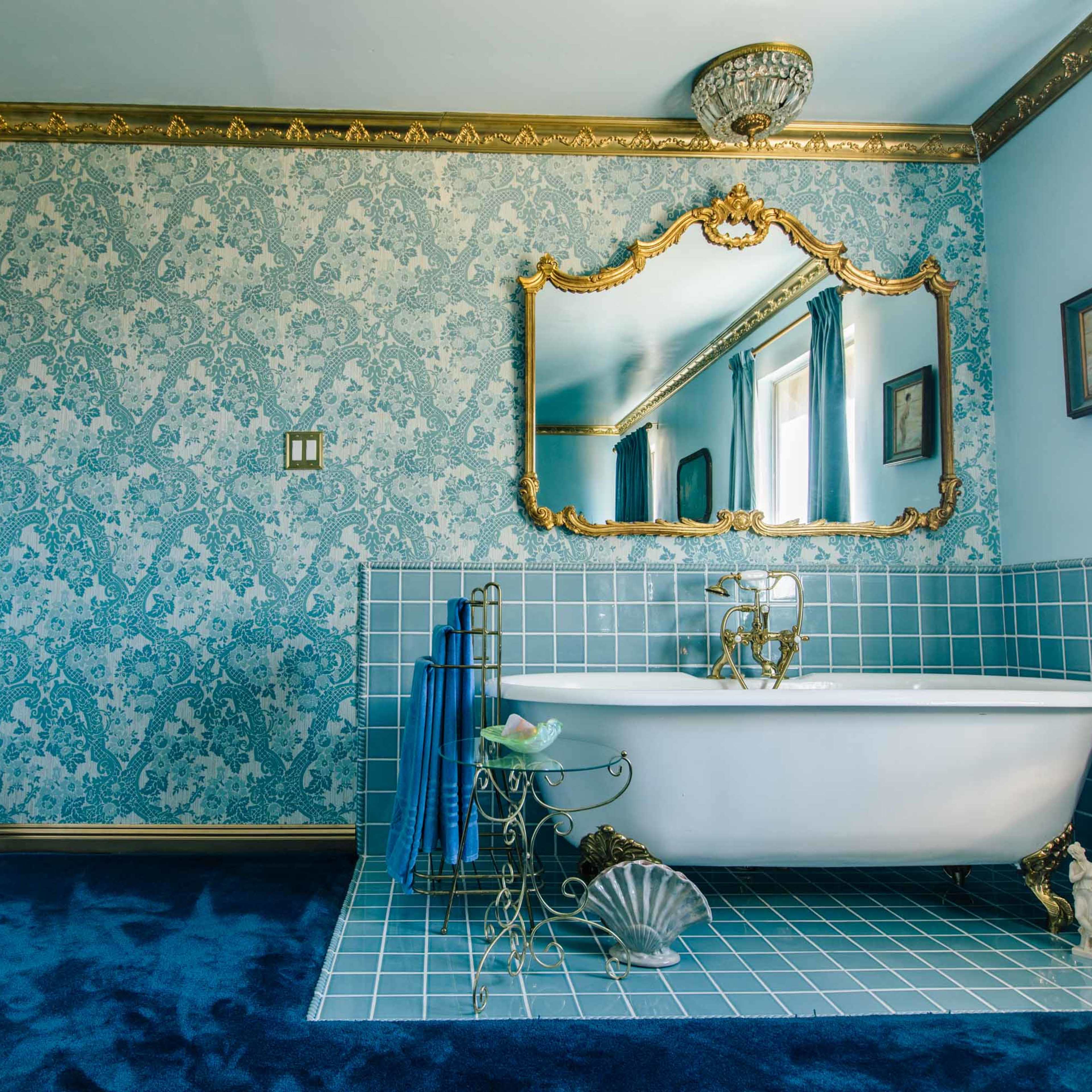 A brightly lit bathroom featuring a freestanding white bathtub, blue tiled walls, and decorative vintage elements.