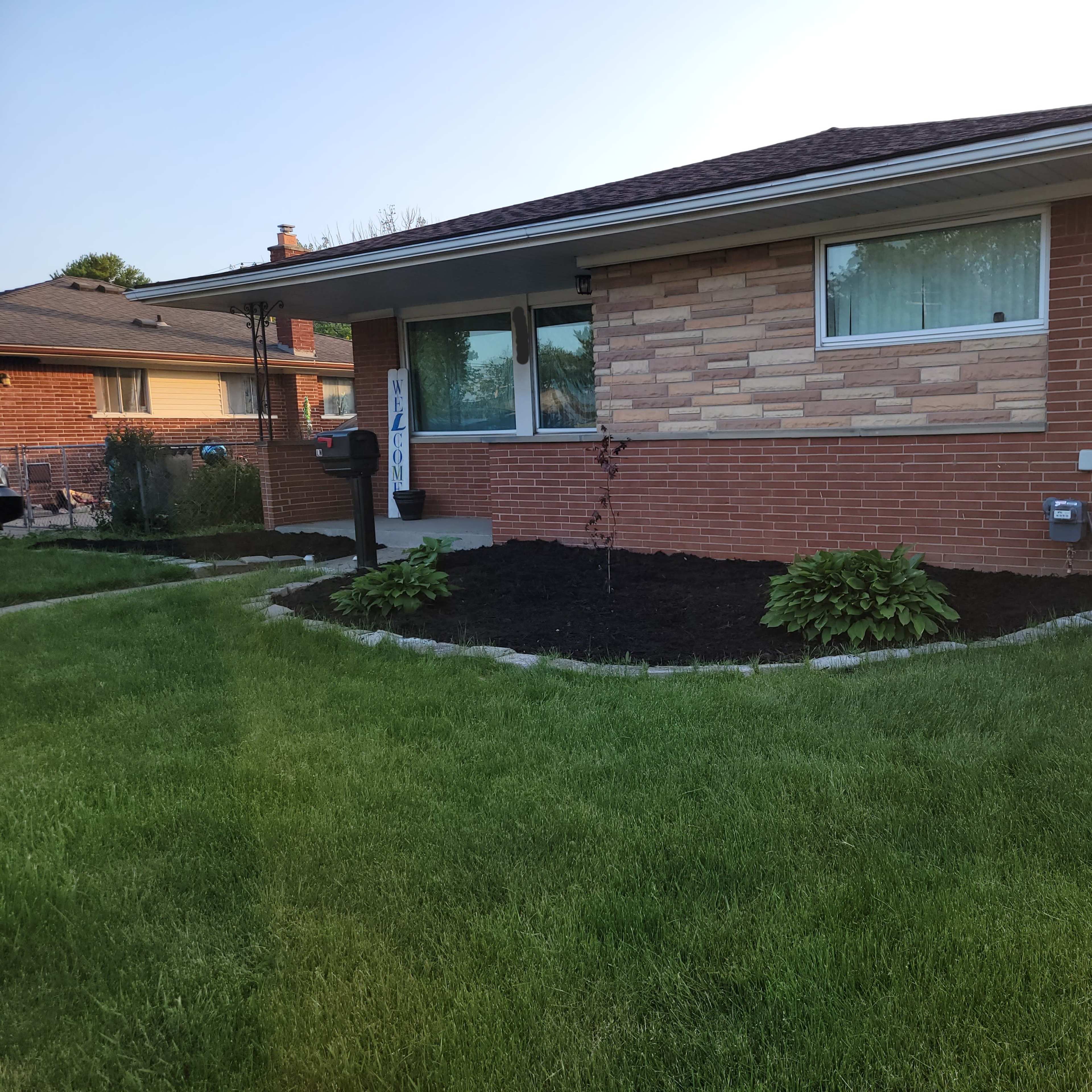 A single-story brick house with a landscaped front yard featuring trimmed grass and plants along the border.