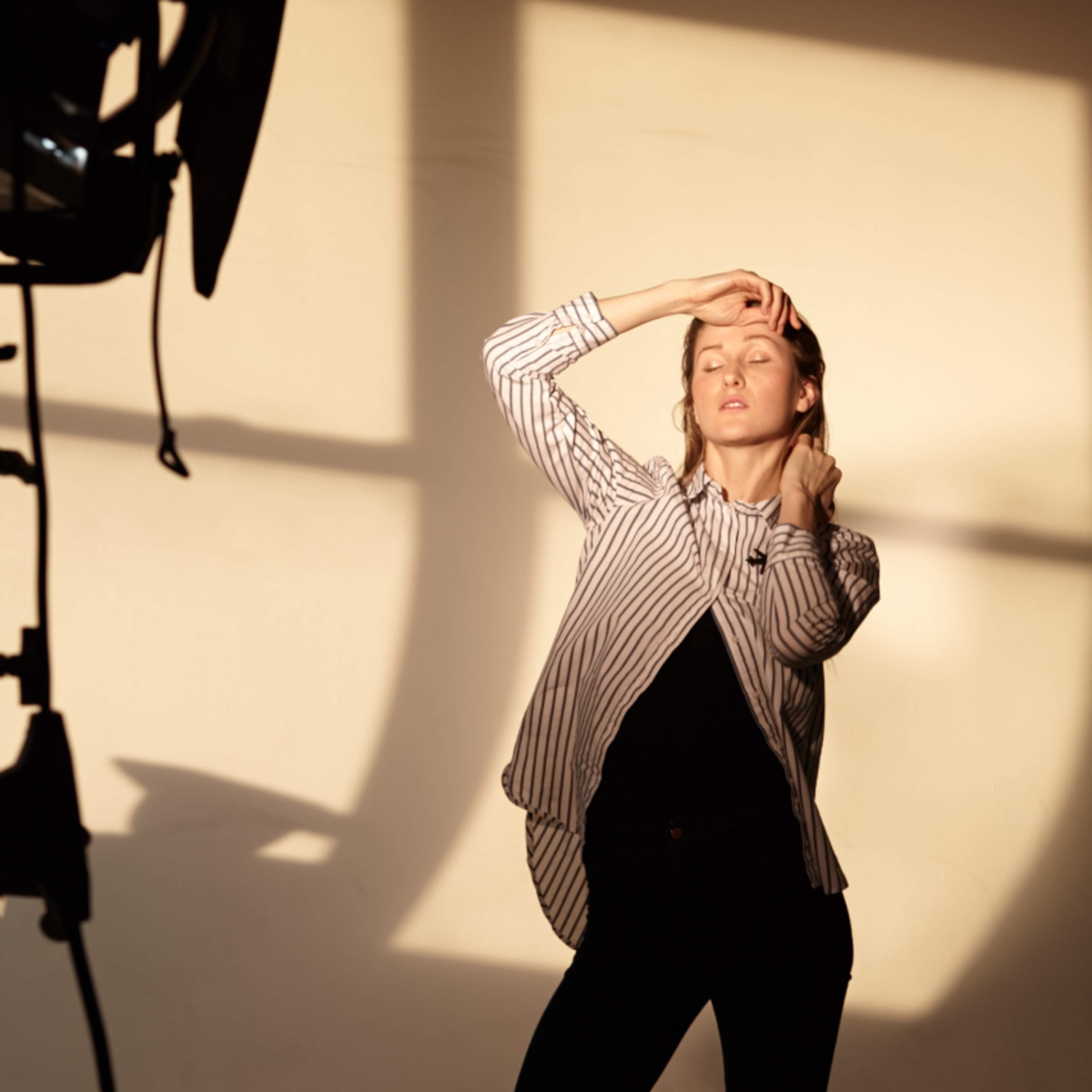 A woman poses in front of a light source, highlighting her silhouette against a plain wall.