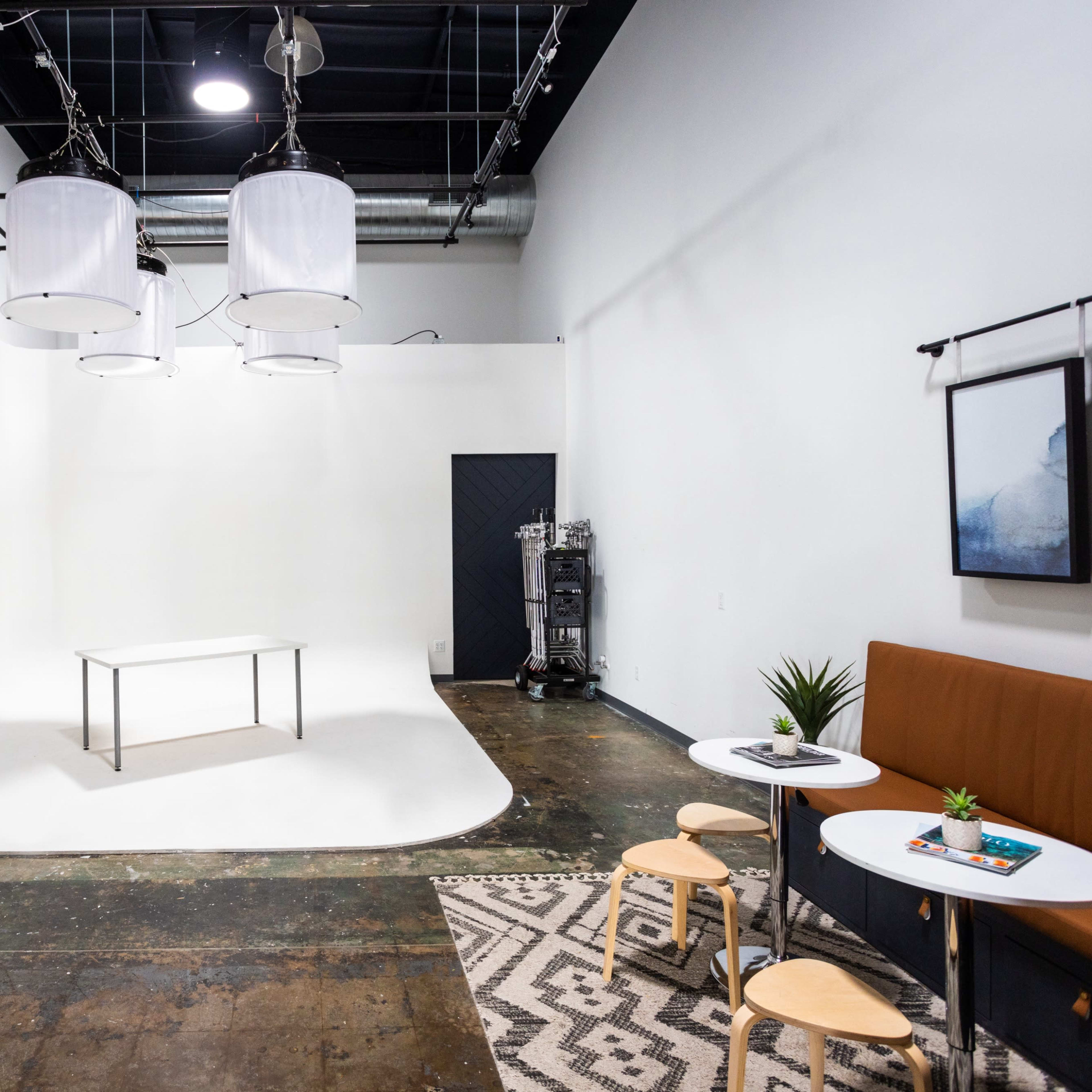 A minimalist photography studio with three hanging lights, a central table, and a seating area featuring a small table and chairs.