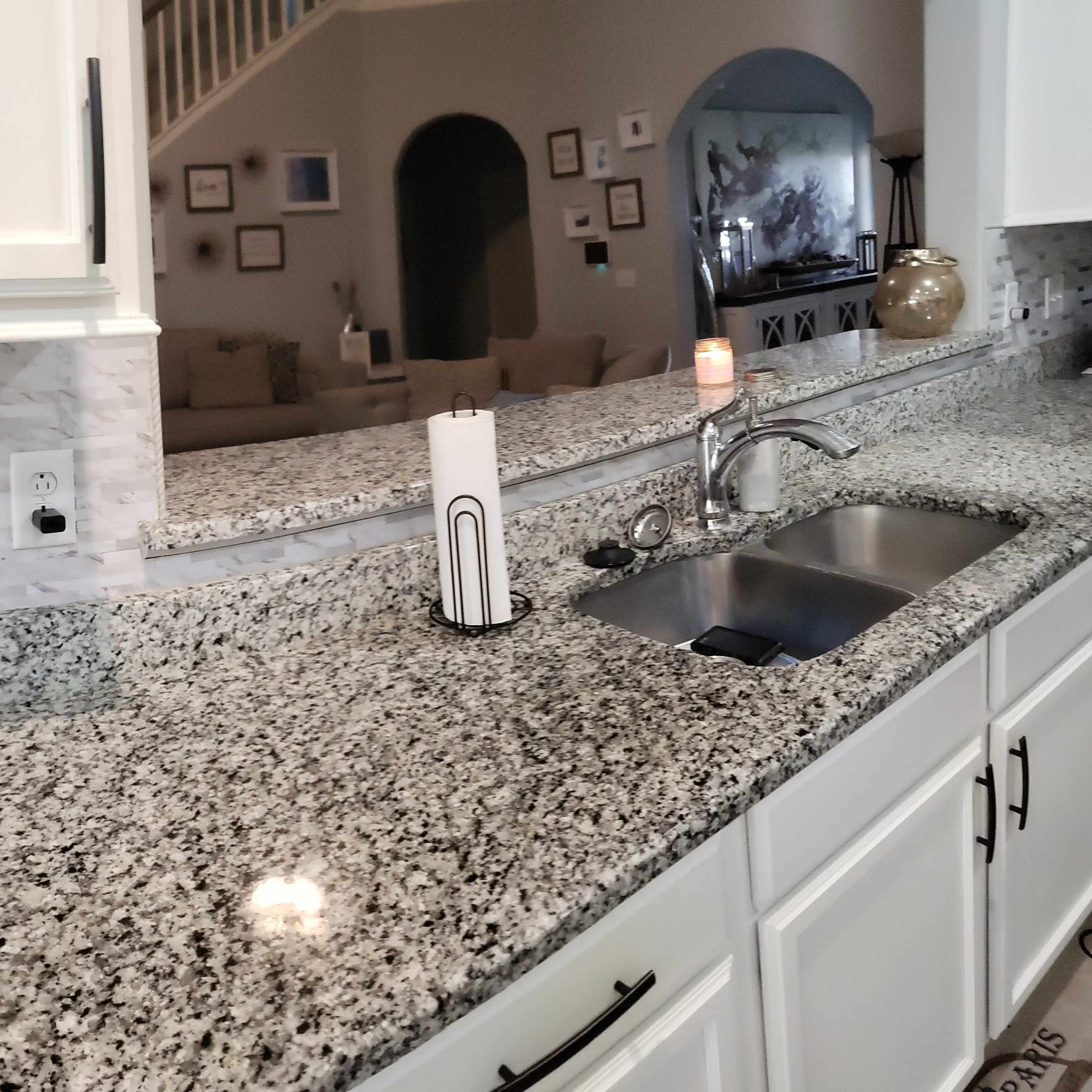 A kitchen with granite countertops, a sink, and a view into a living area with a couch and decorative elements.