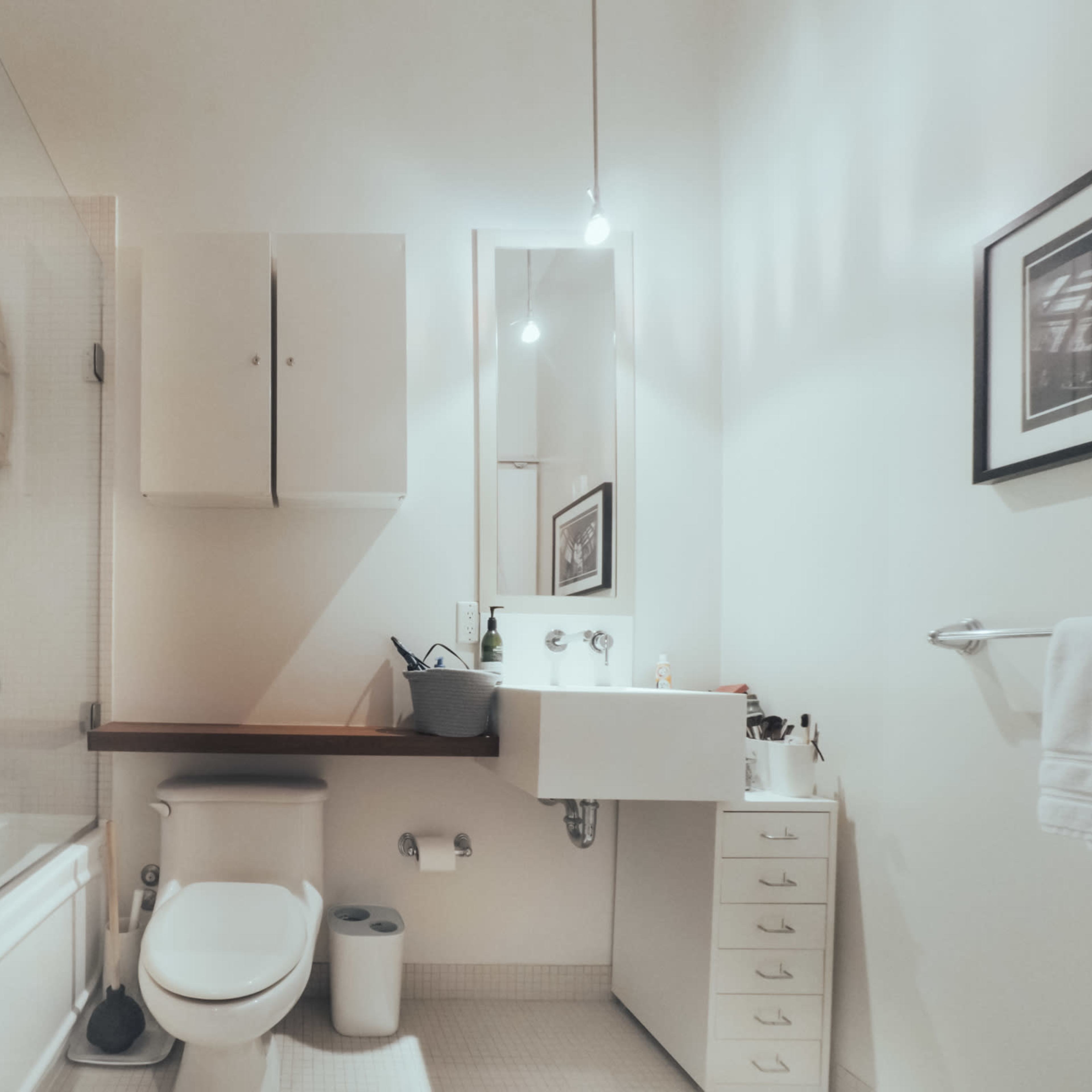 A modern bathroom featuring a glass shower, a white toilet, a sink with a wall-mounted mirror, and cabinets for storage.