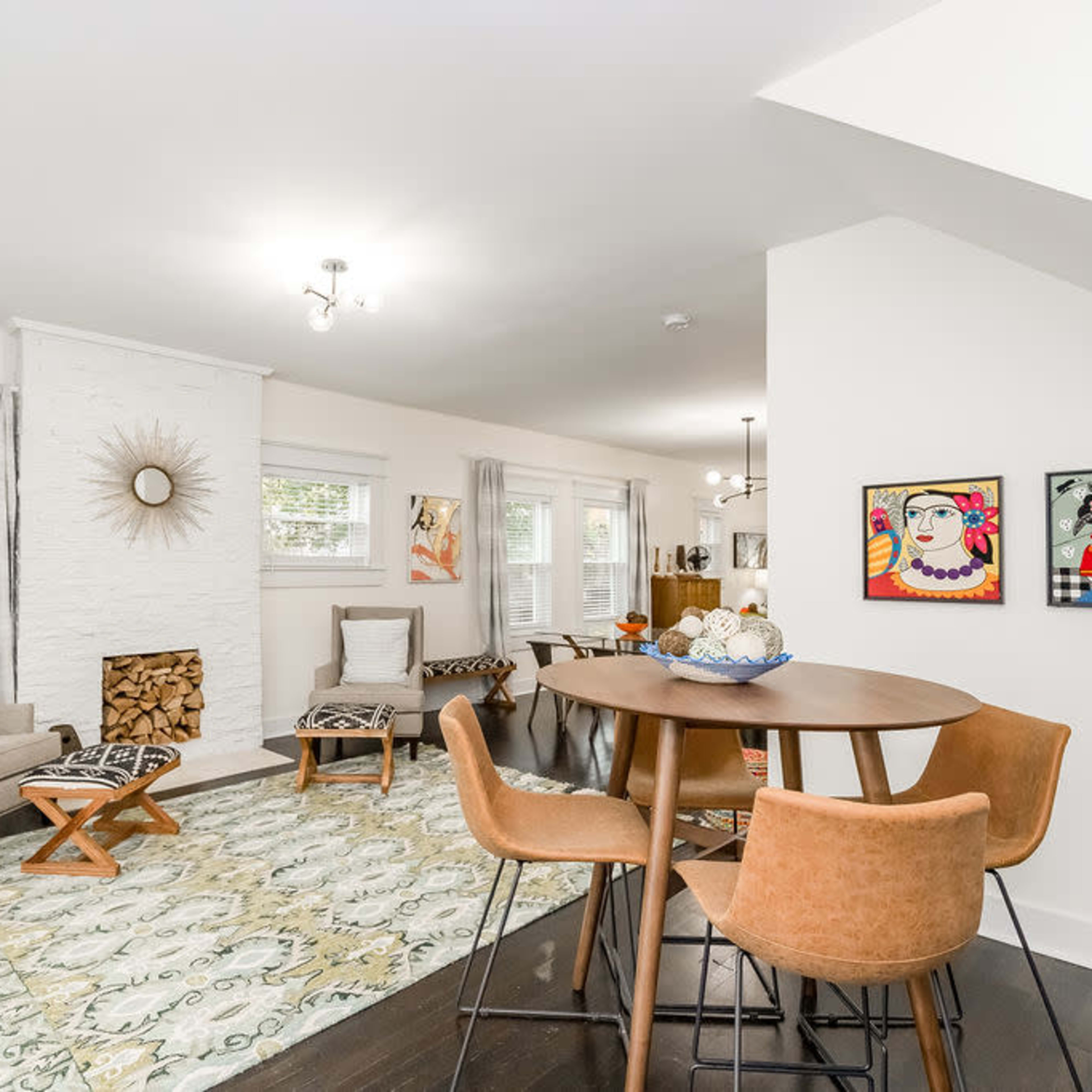 A bright and modern living space featuring a dining table with brown chairs, a cozy seating area, and a white-washed fireplace adorned with artwork and decorative items.