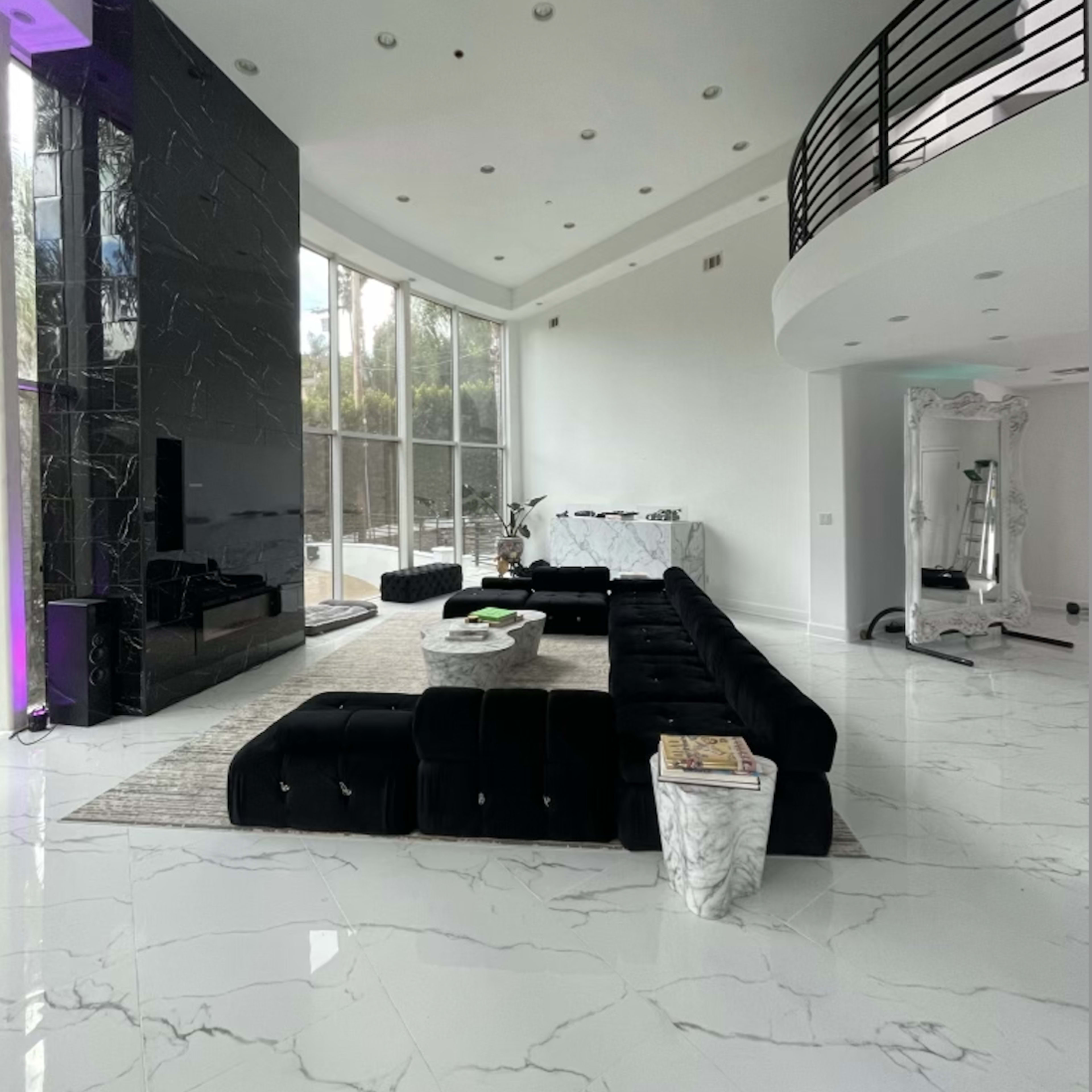A modern living room with a large black sectional sofa, a marble floor, and large windows letting in natural light.