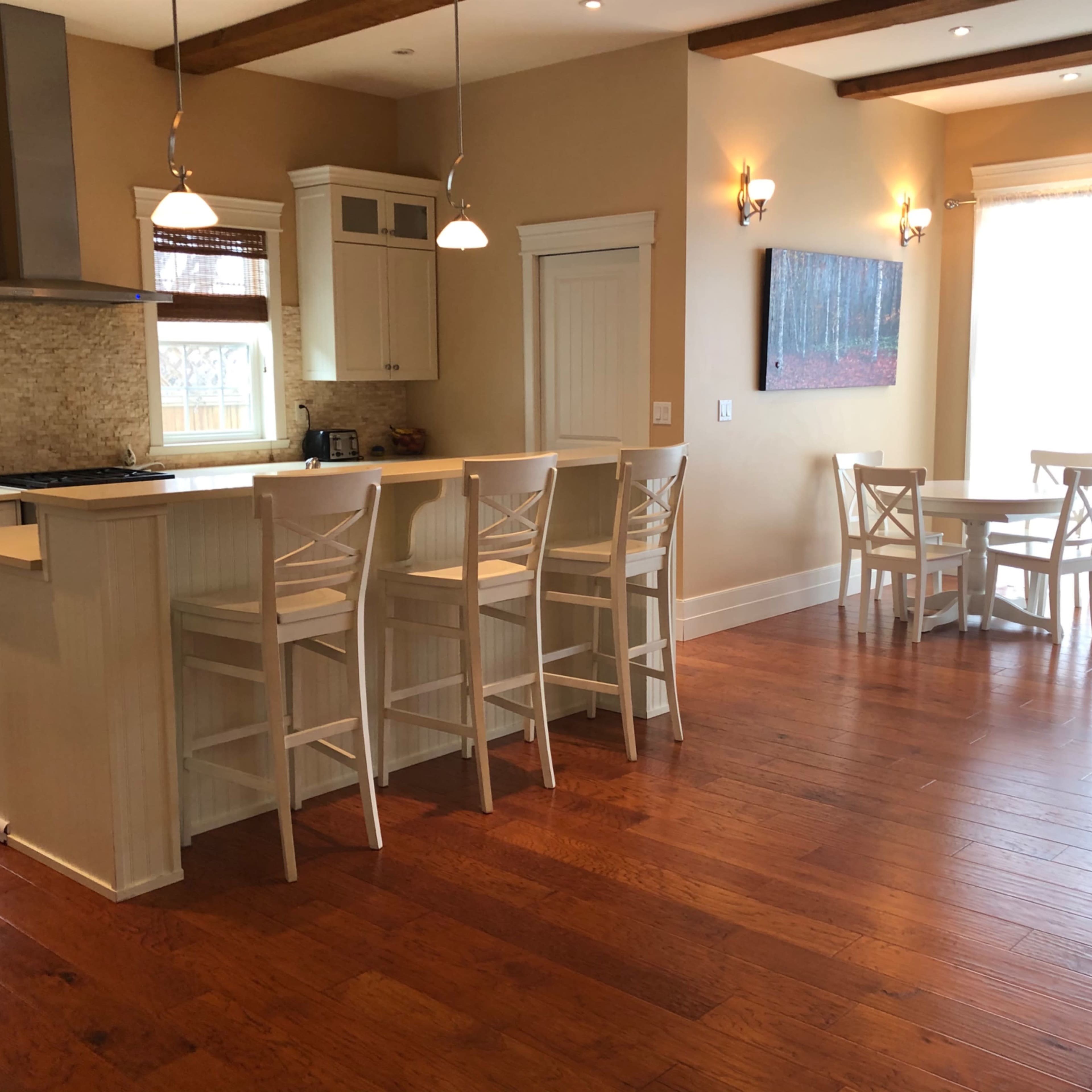 A modern kitchen with a central island and four bar stools, adjacent to a dining area that features a small round table and two chairs, all set in a room with hardwood flooring.