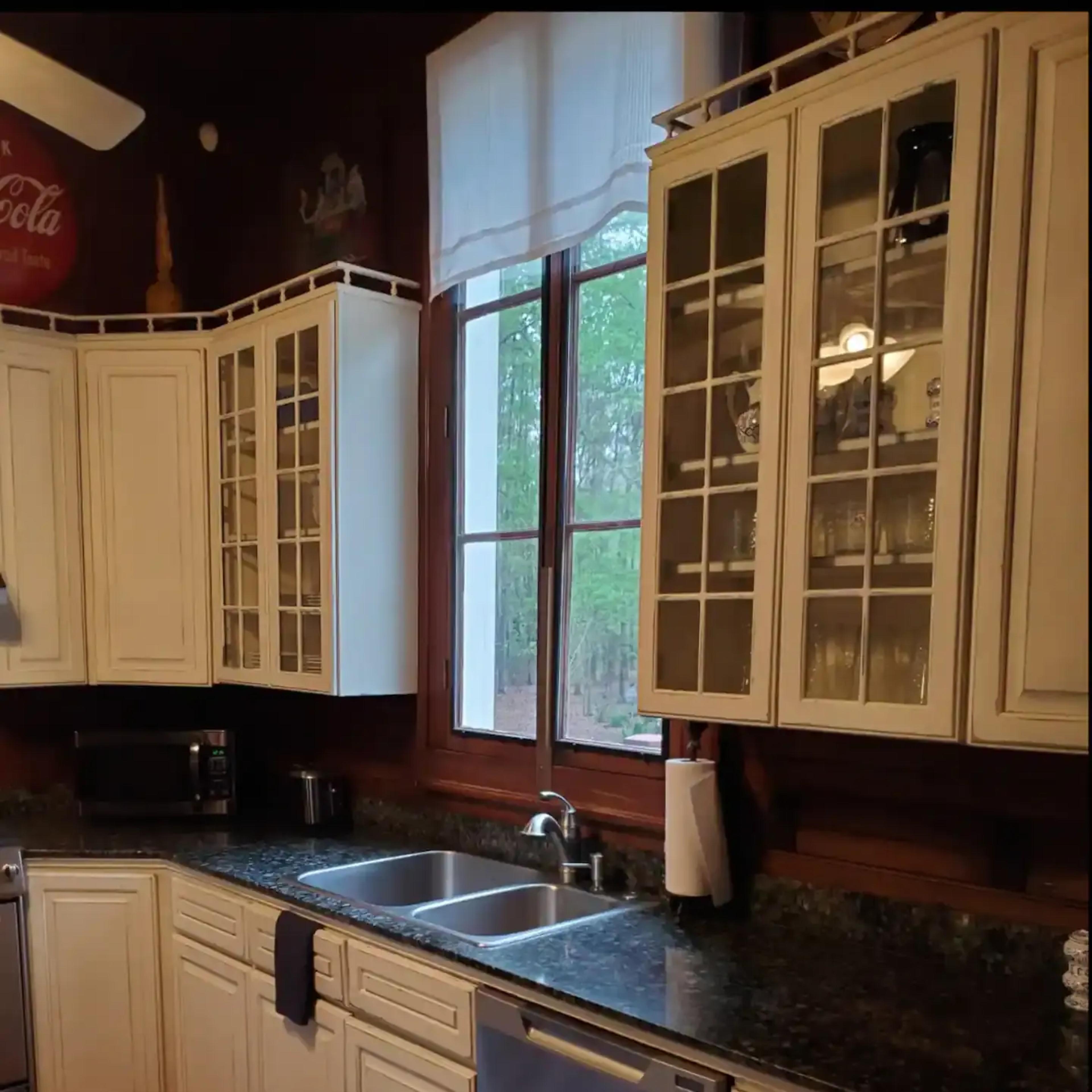 A kitchen with white cabinetry, a dark countertop, a sink below a large window, and modern appliances.
