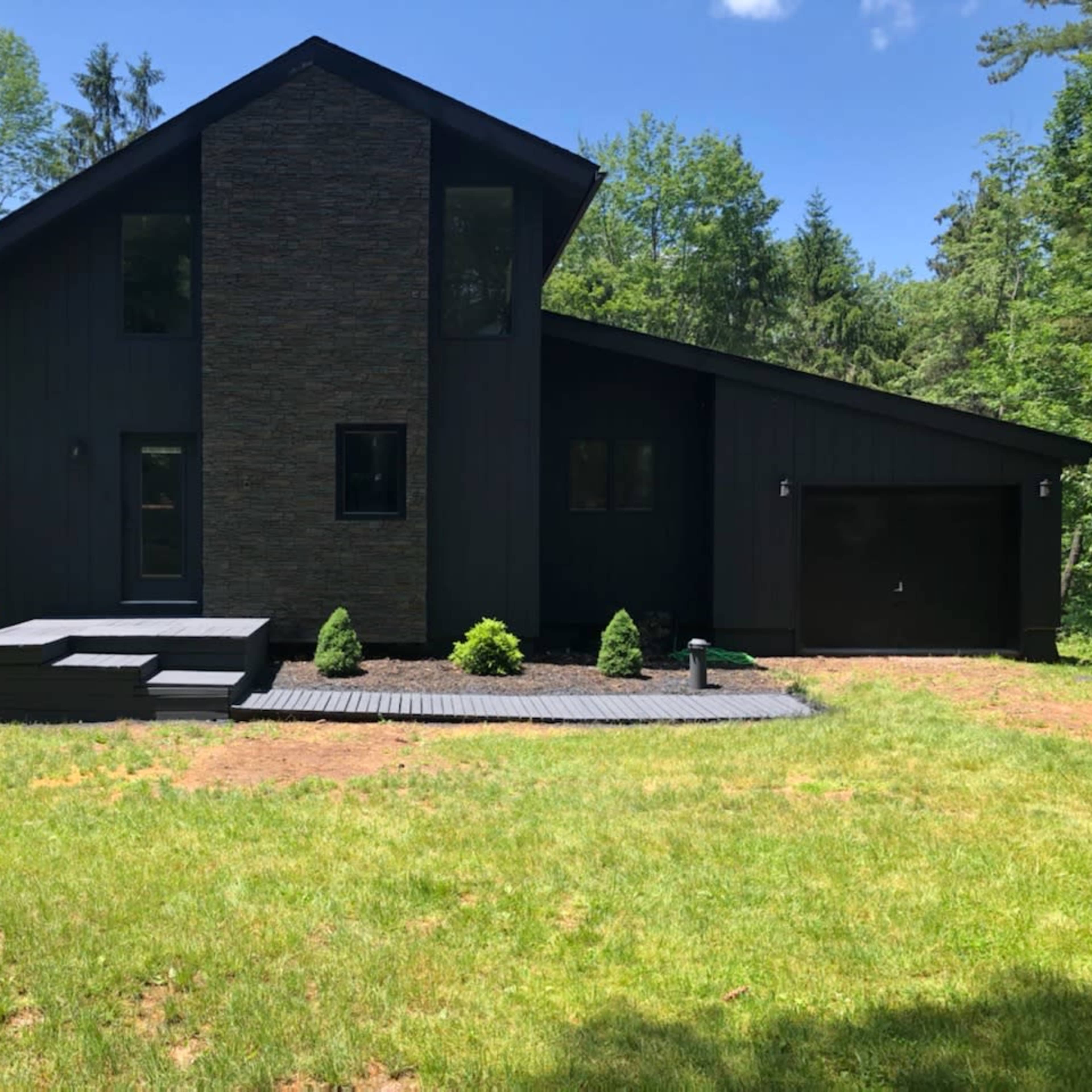A modern black house with a stone accent wall is surrounded by green grass and trees.