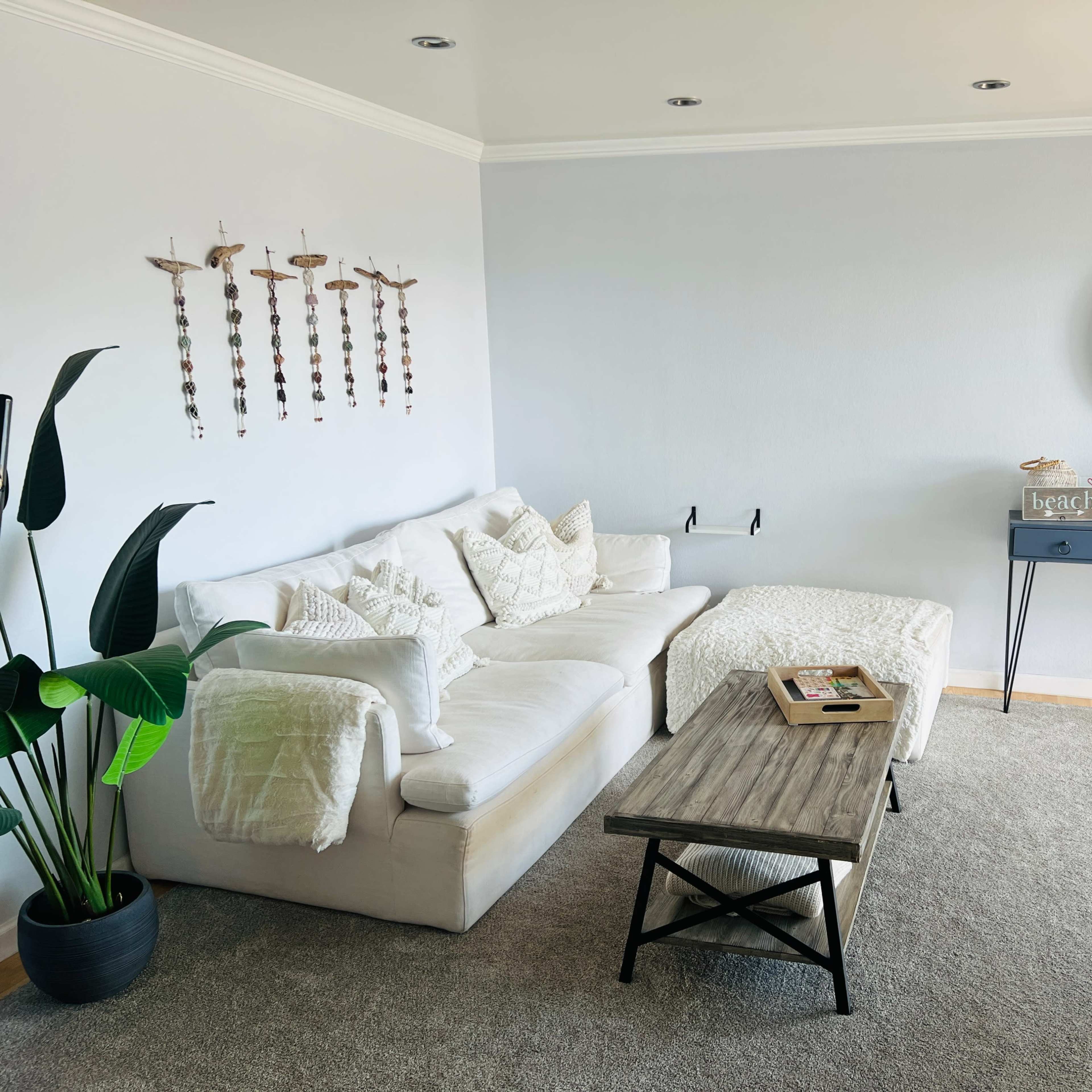 A modern living room with a white sectional sofa, a wooden coffee table, a decorative wall mirror, and potted plants.