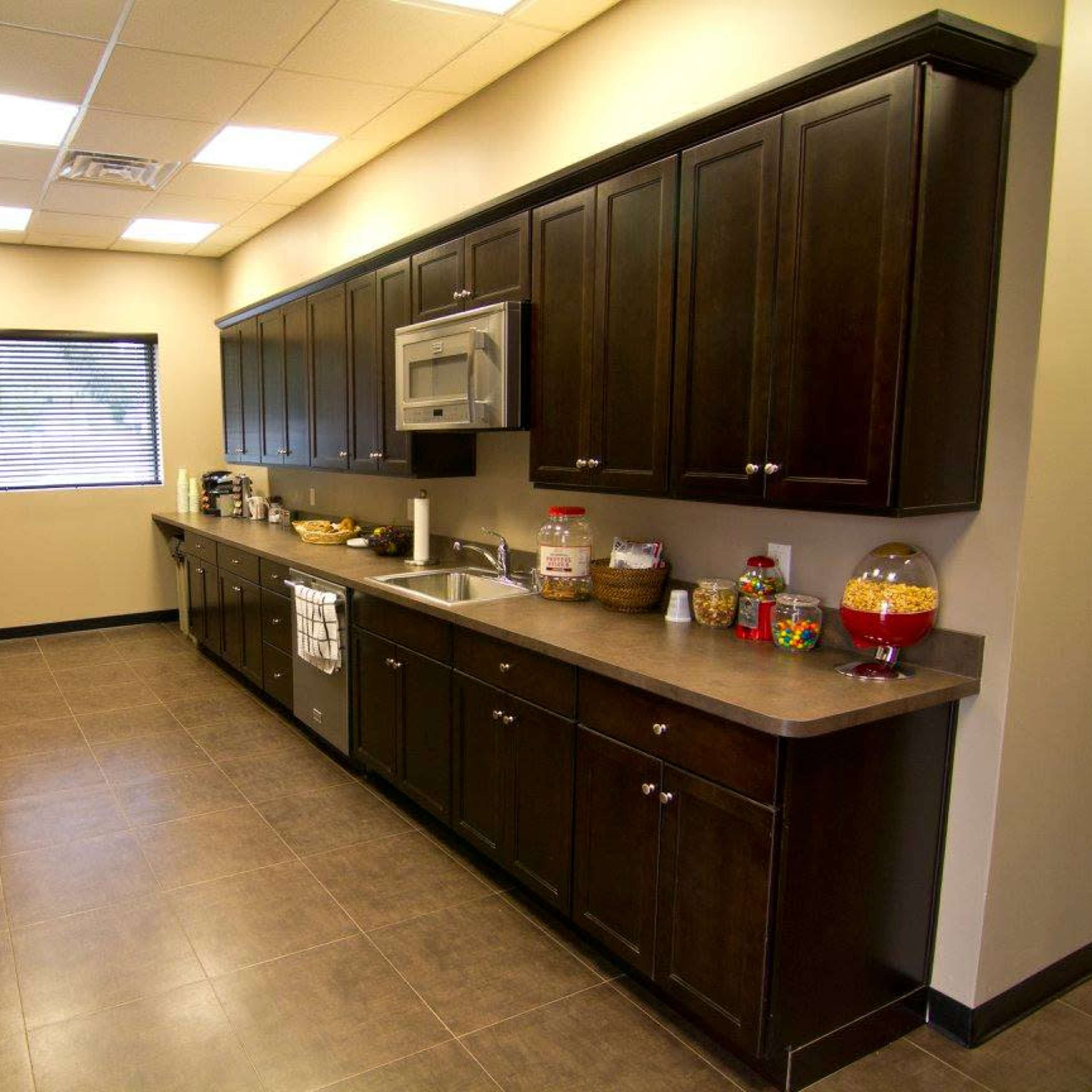 A modern kitchen with dark wooden cabinets, a countertop, and stainless steel appliances, illuminated by overhead lighting.