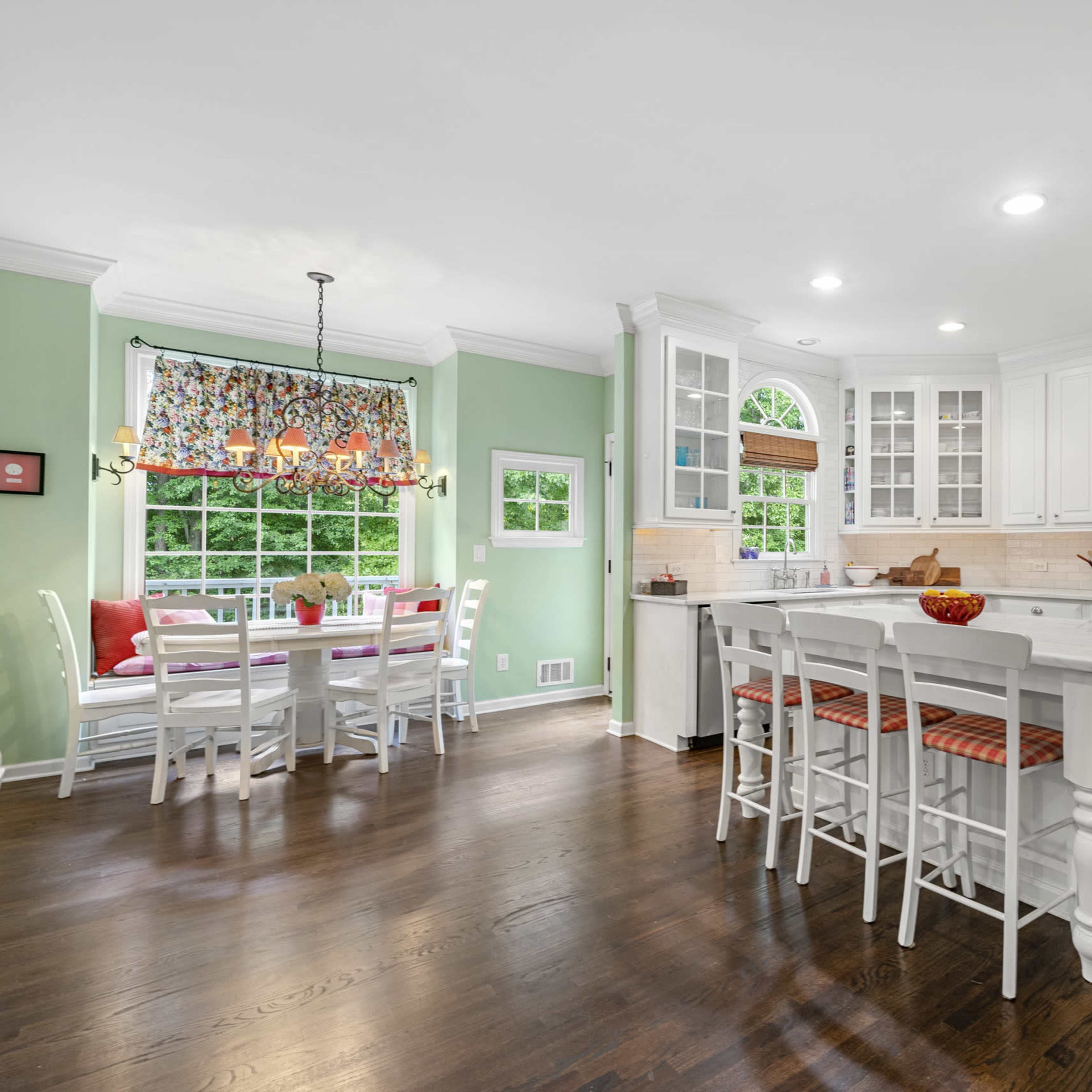 A spacious kitchen with white cabinets, a central island with seating, and a cozy dining area featuring a large window and colorful window treatments.