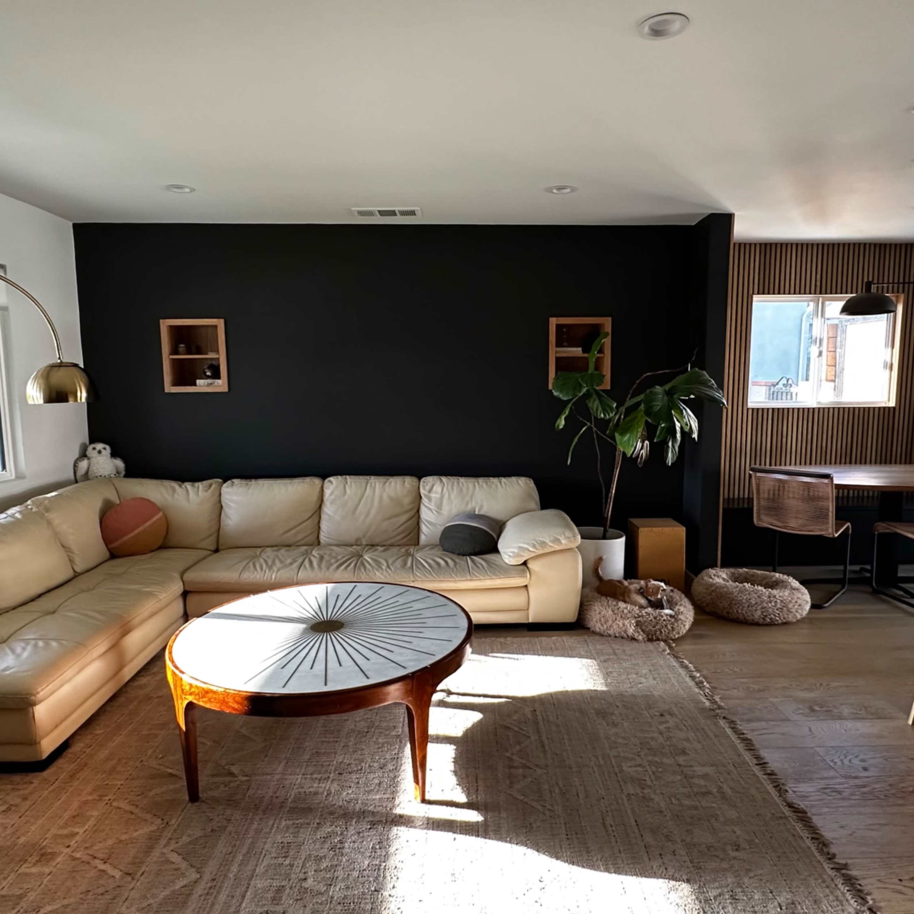 A bright, modern living space featuring a light-colored sectional sofa, a round coffee table, and a dining area with wooden chairs and a table.