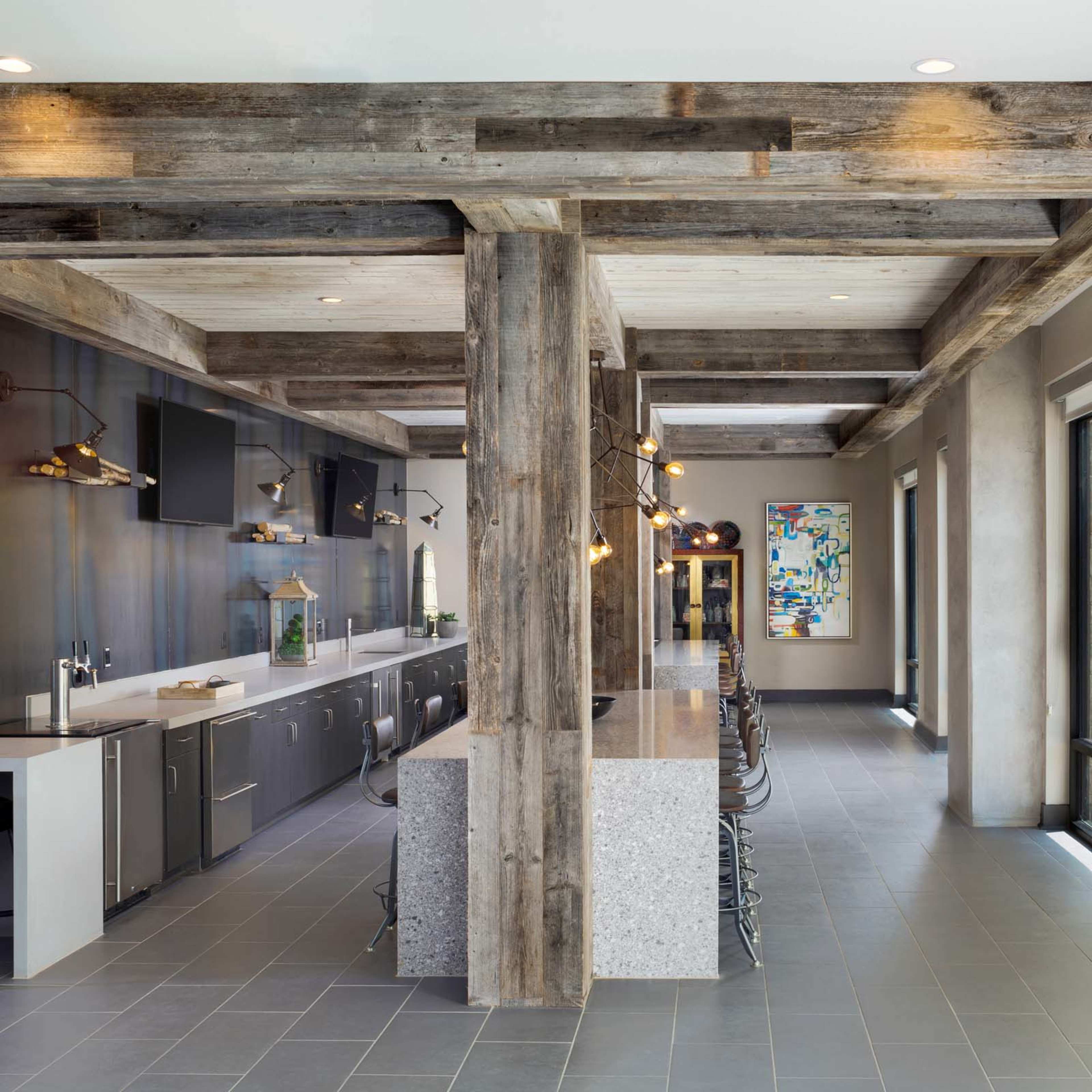 A modern kitchen area features wooden beams, sleek countertops, and large windows that allow natural light to fill the space.