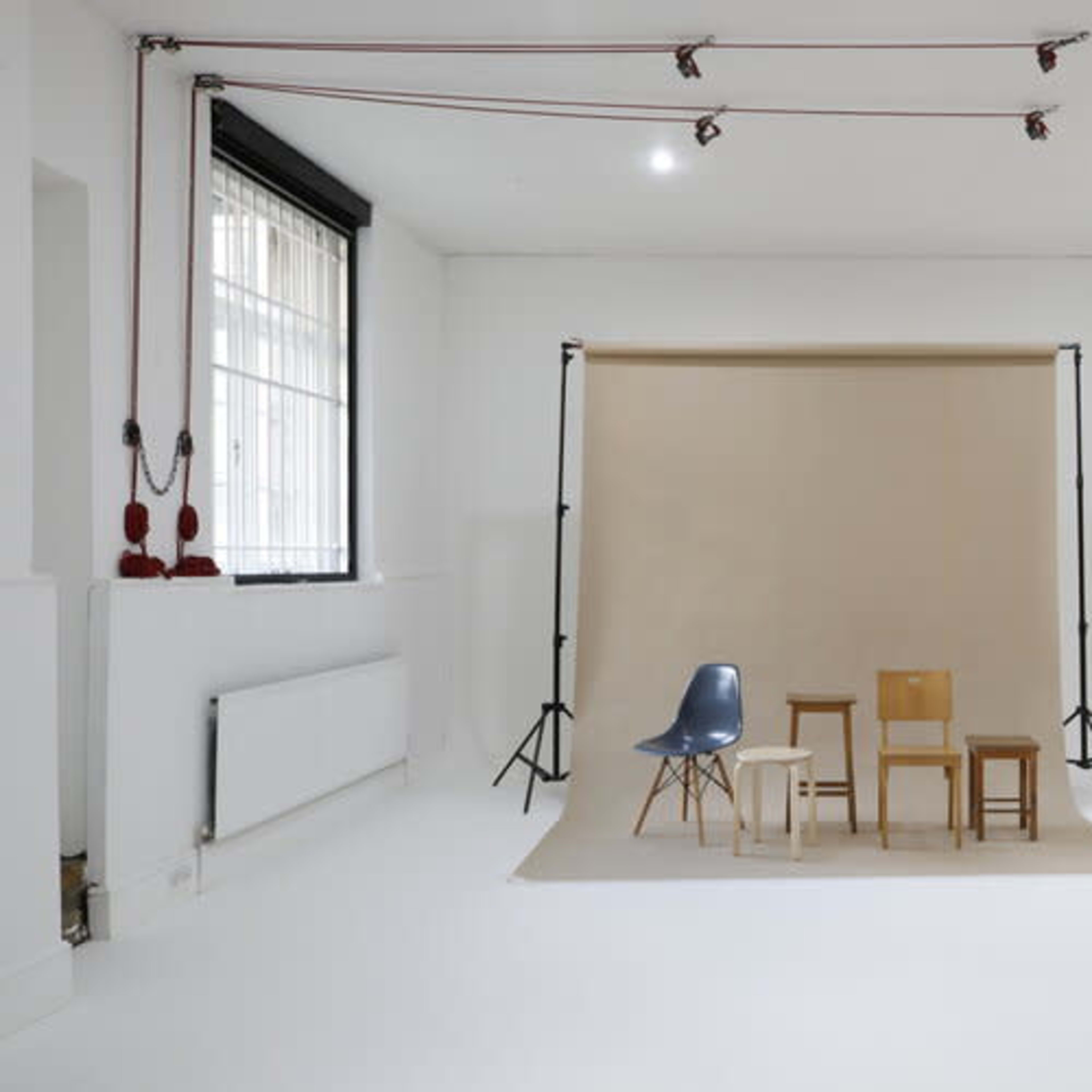 A minimalist studio space with three chairs arranged in front of a beige backdrop.