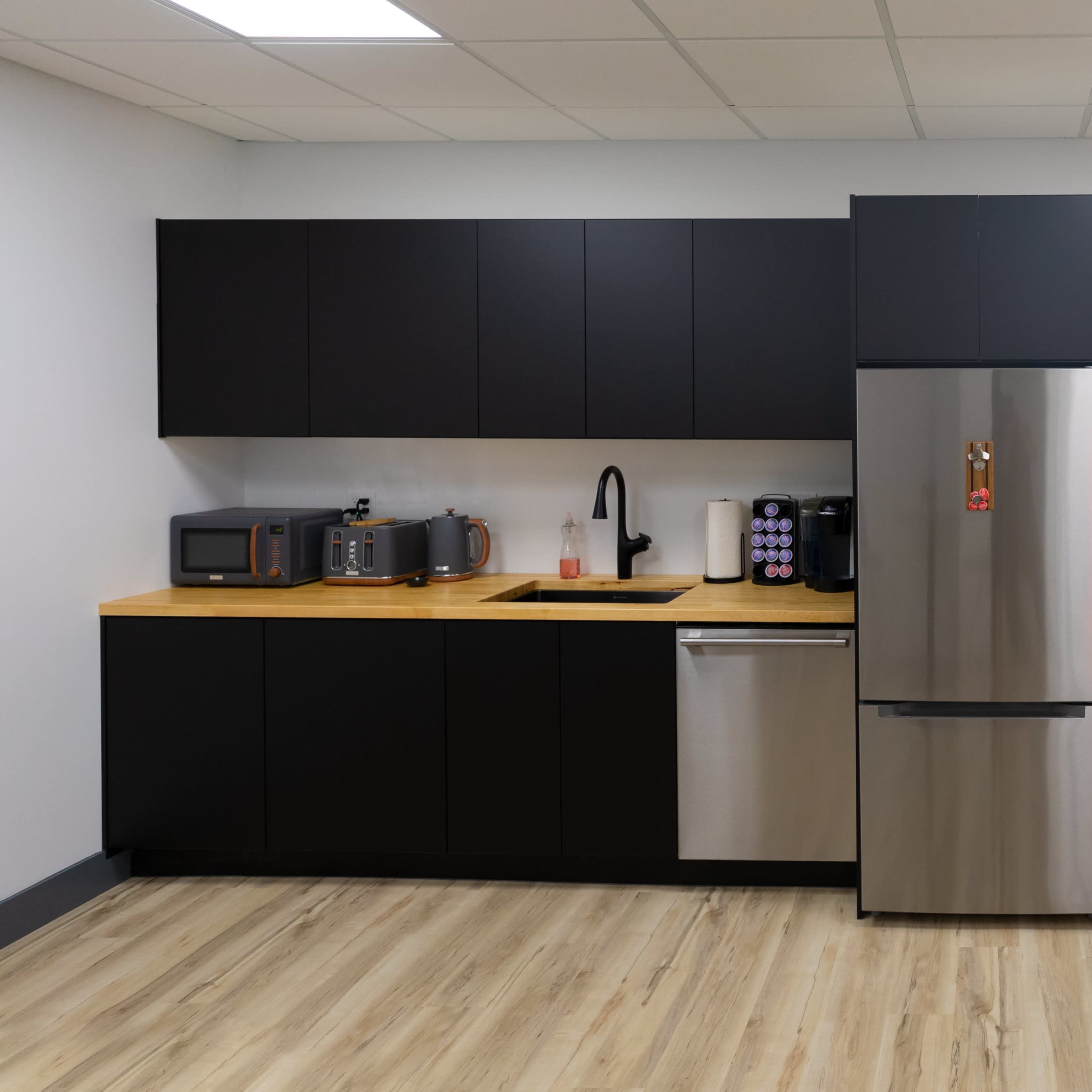 A modern kitchen with black cabinetry, stainless steel appliances, and a wooden countertop.
