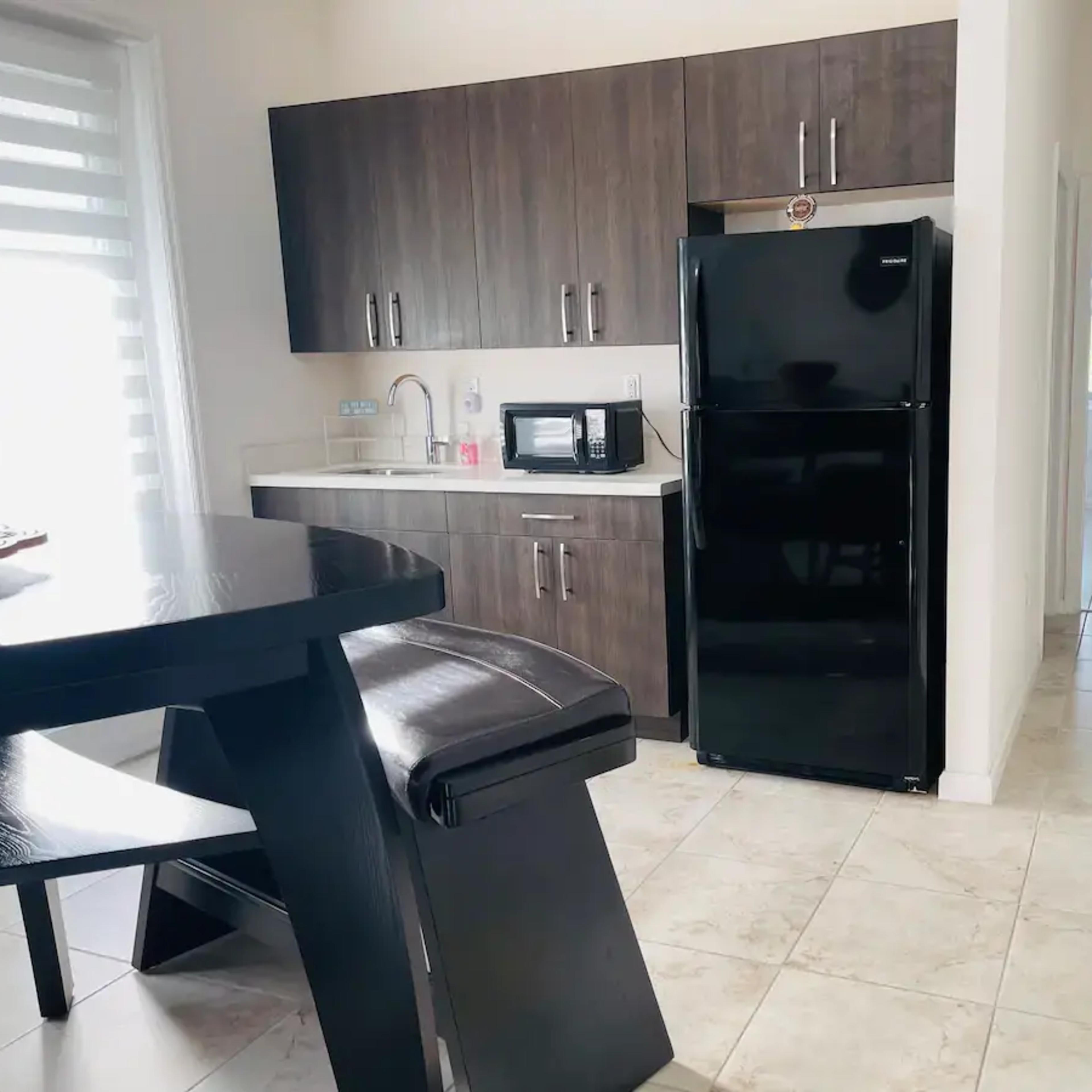A modern kitchen features dark wooden cabinetry, a black refrigerator, and a microwave, with a dining table positioned nearby.