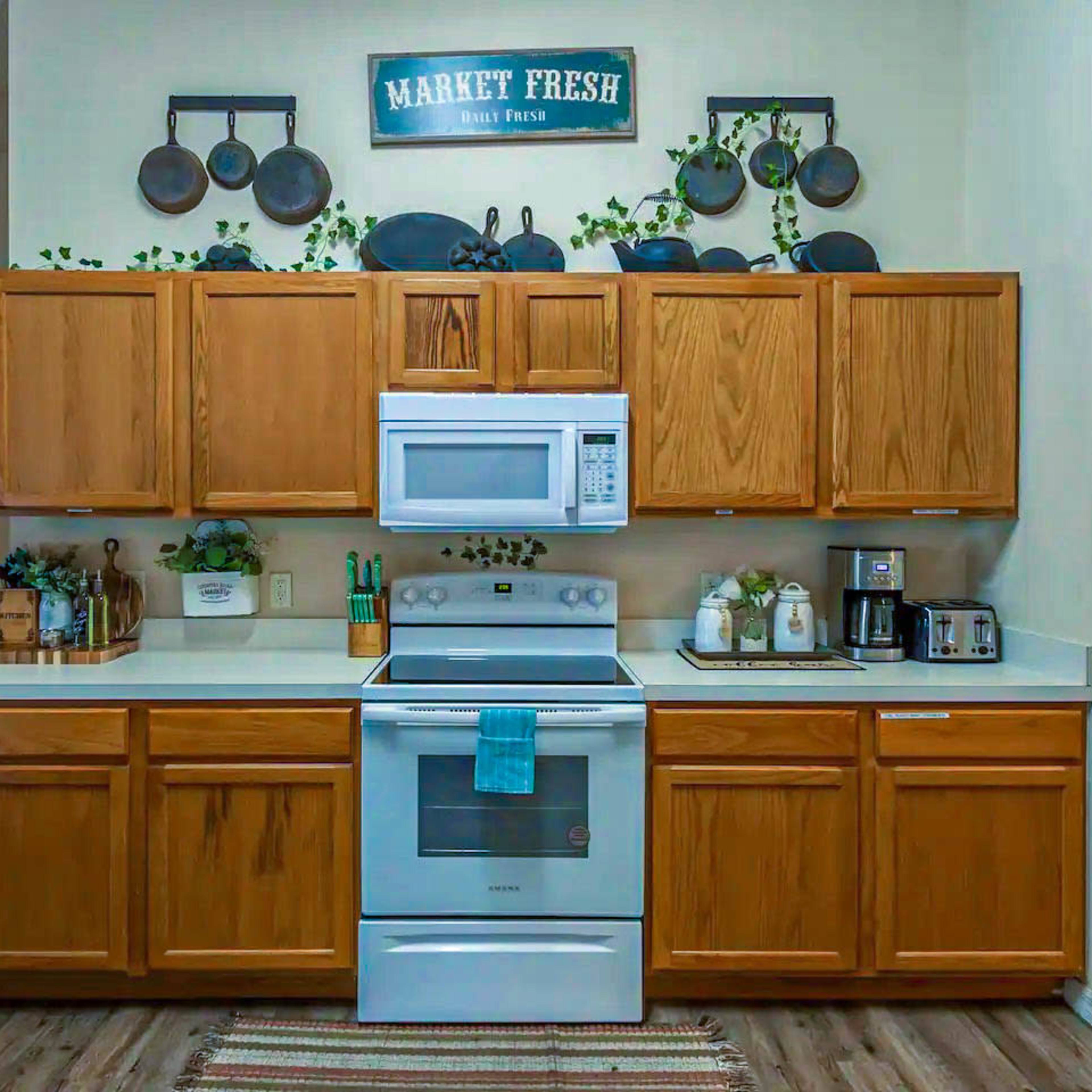A kitchen with wooden cabinets, a white stove and microwave, and decorative items including plants and kitchenware on the countertops.