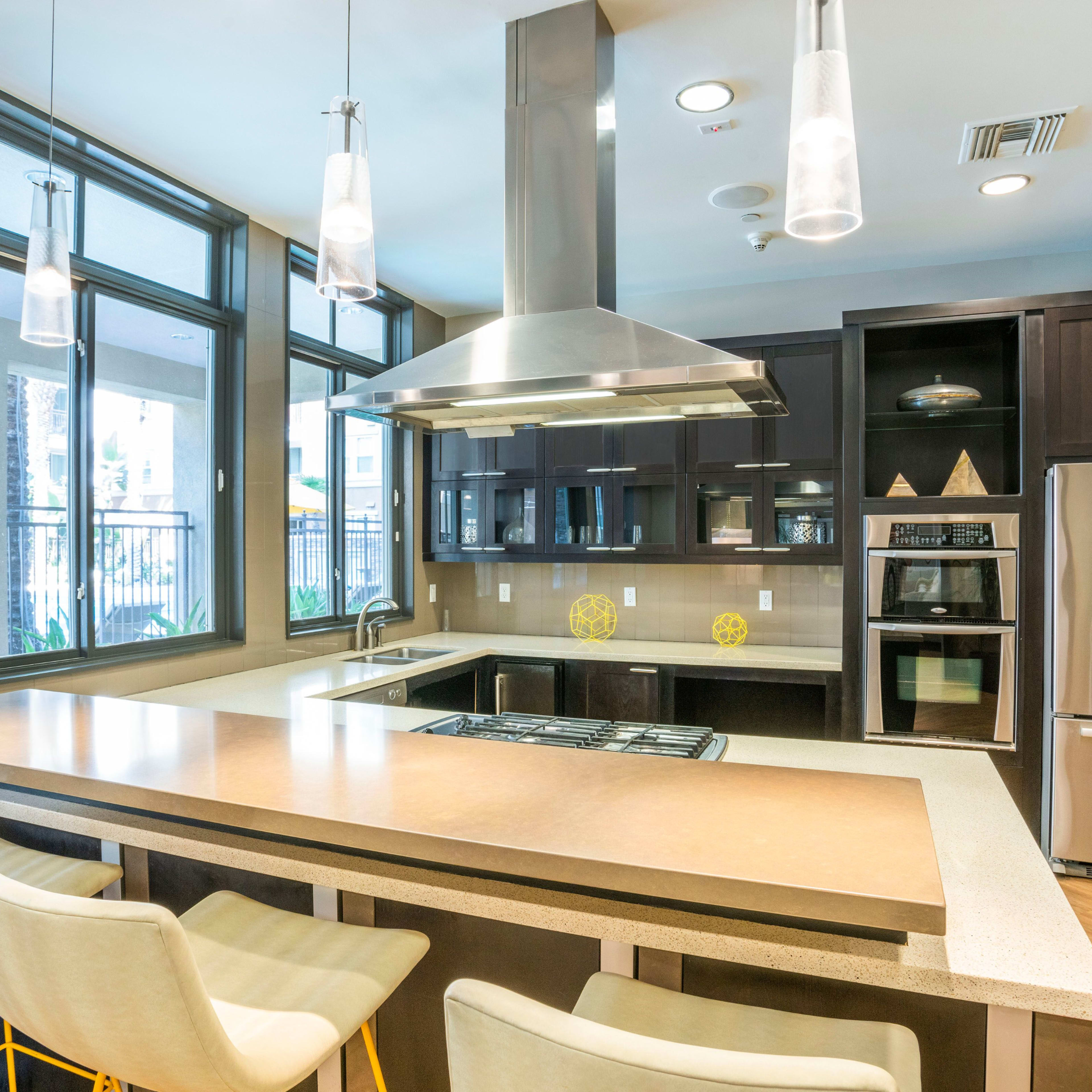 A modern kitchen features a central island with seating, stainless steel appliances, and large windows that provide natural light.