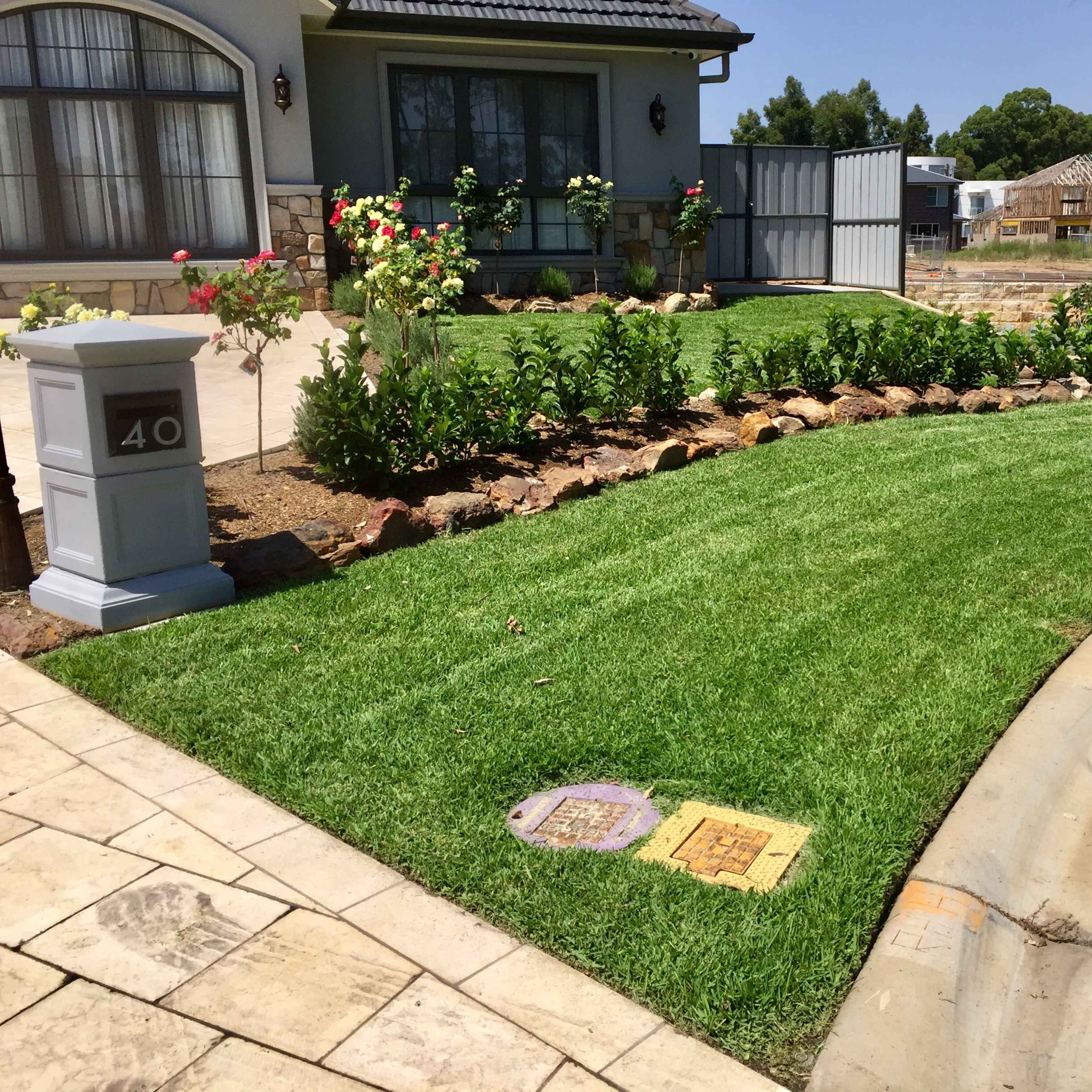 A well-manicured front yard with a neatly edged lawn, bordered by flower beds and a stone pathway in front of a house.