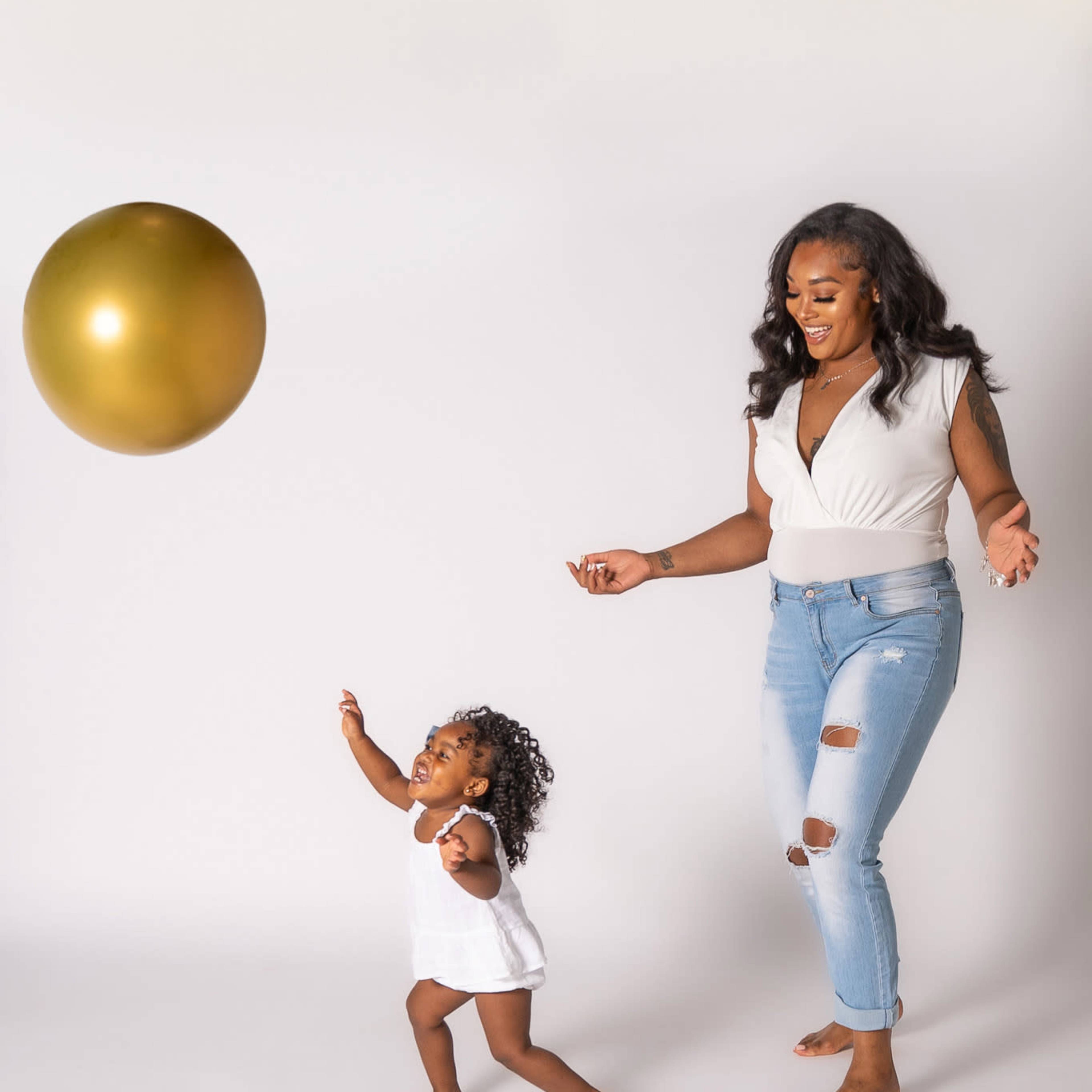 A child runs excitedly towards a large gold balloon while an adult stands nearby, smiling.