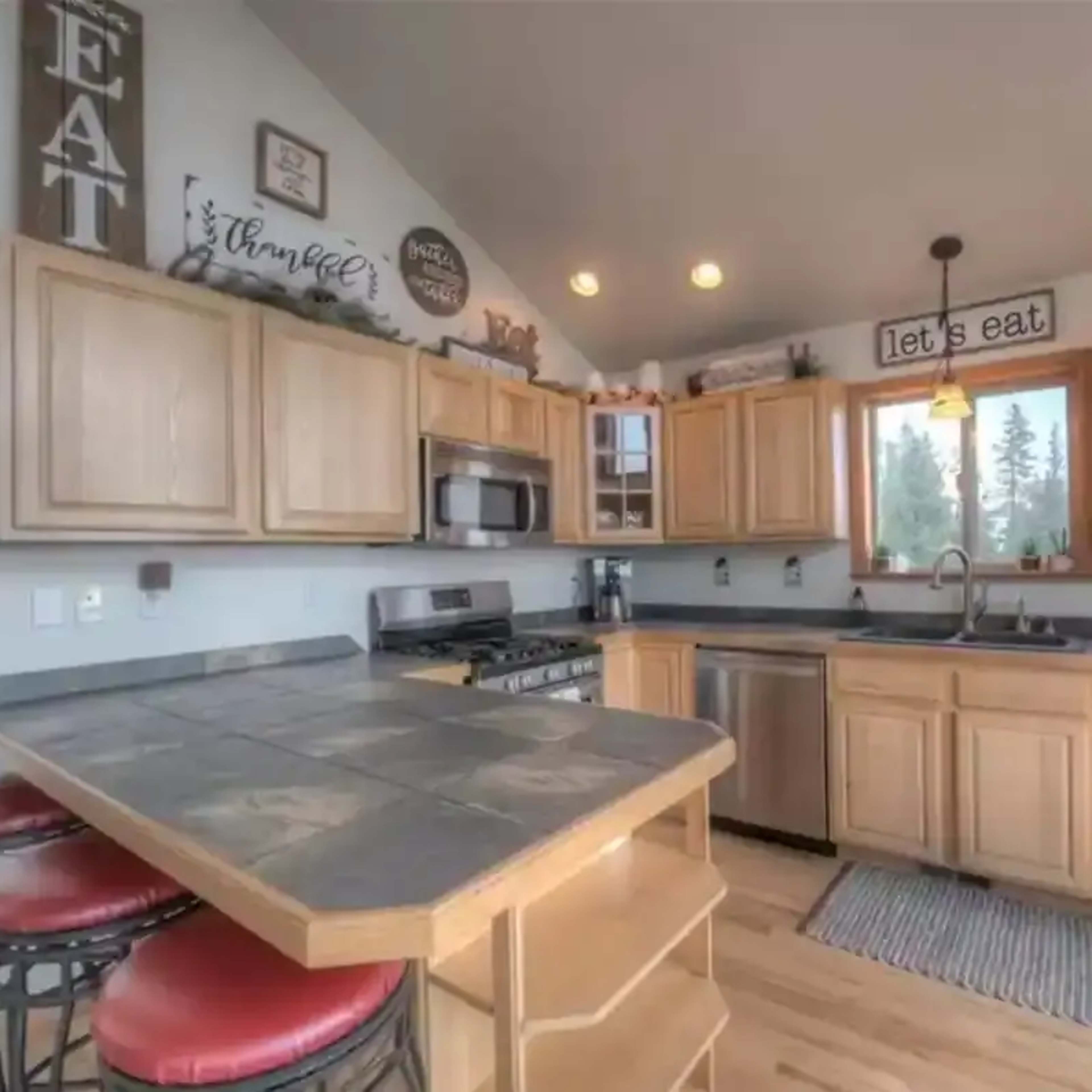 A kitchen features wooden cabinetry, stainless steel appliances, and a central island with red bar stools.