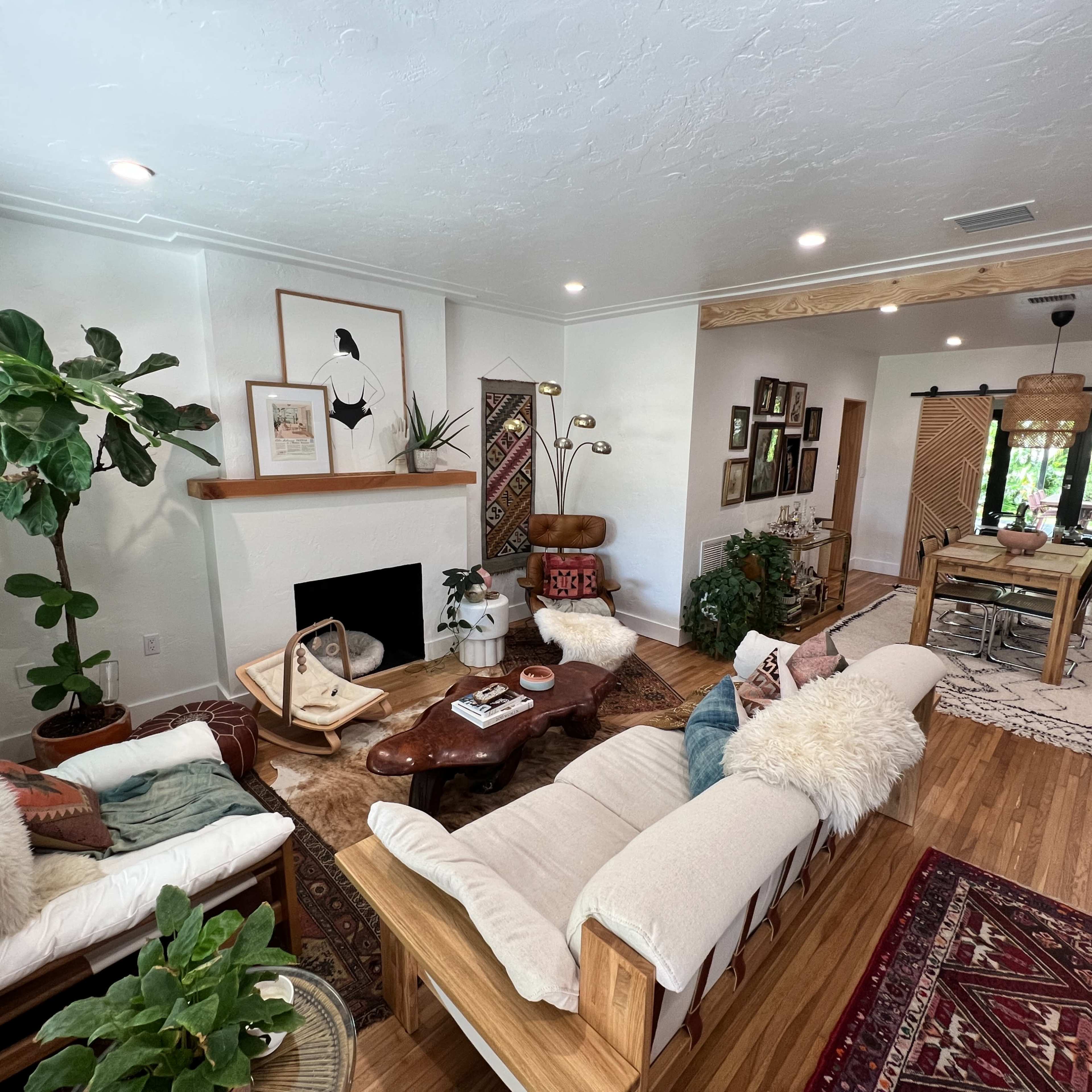 A cozy living room with two sofas, a coffee table, plants, and a dining area in the background.