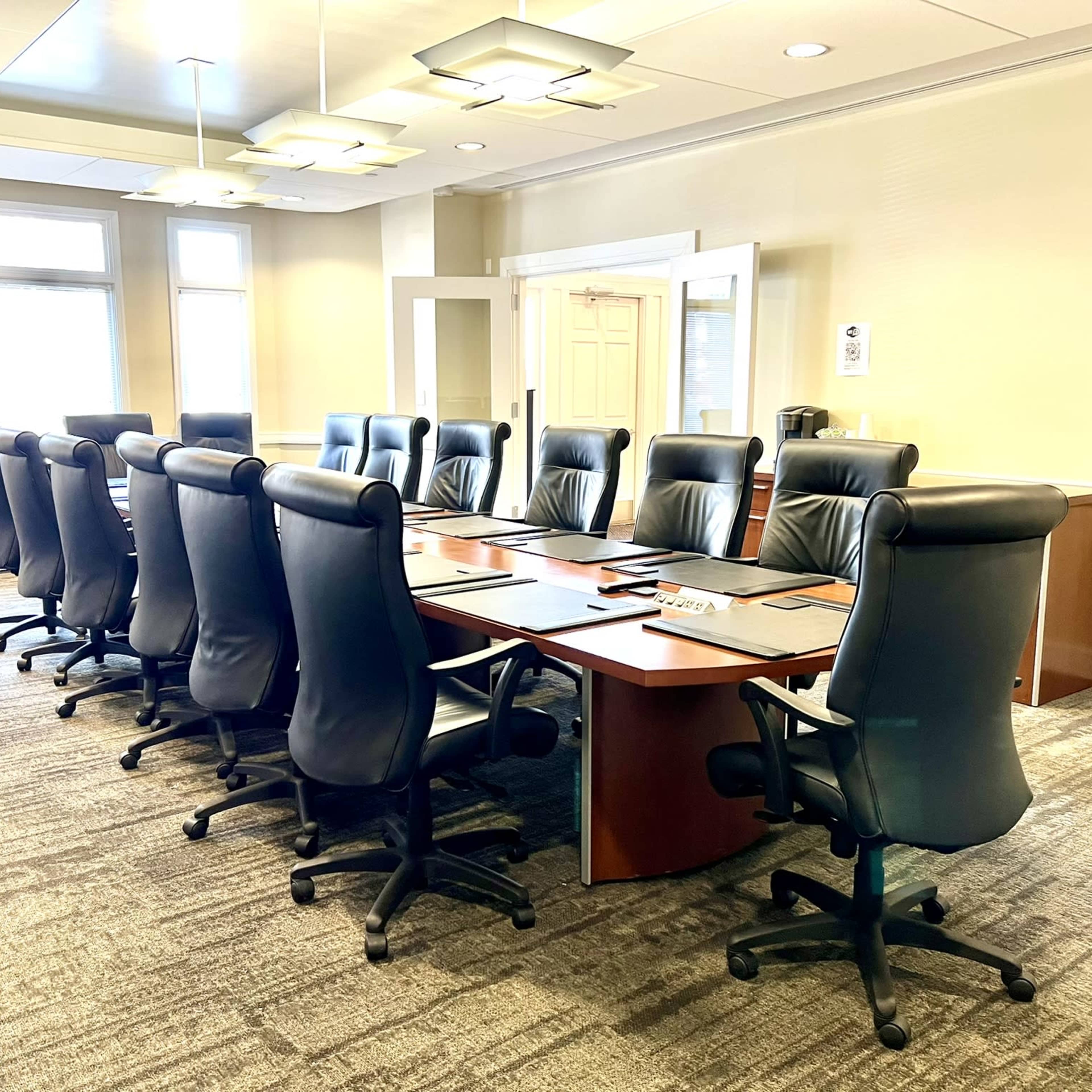 A large conference room with a rectangular table surrounded by leather office chairs and bright overhead lighting.