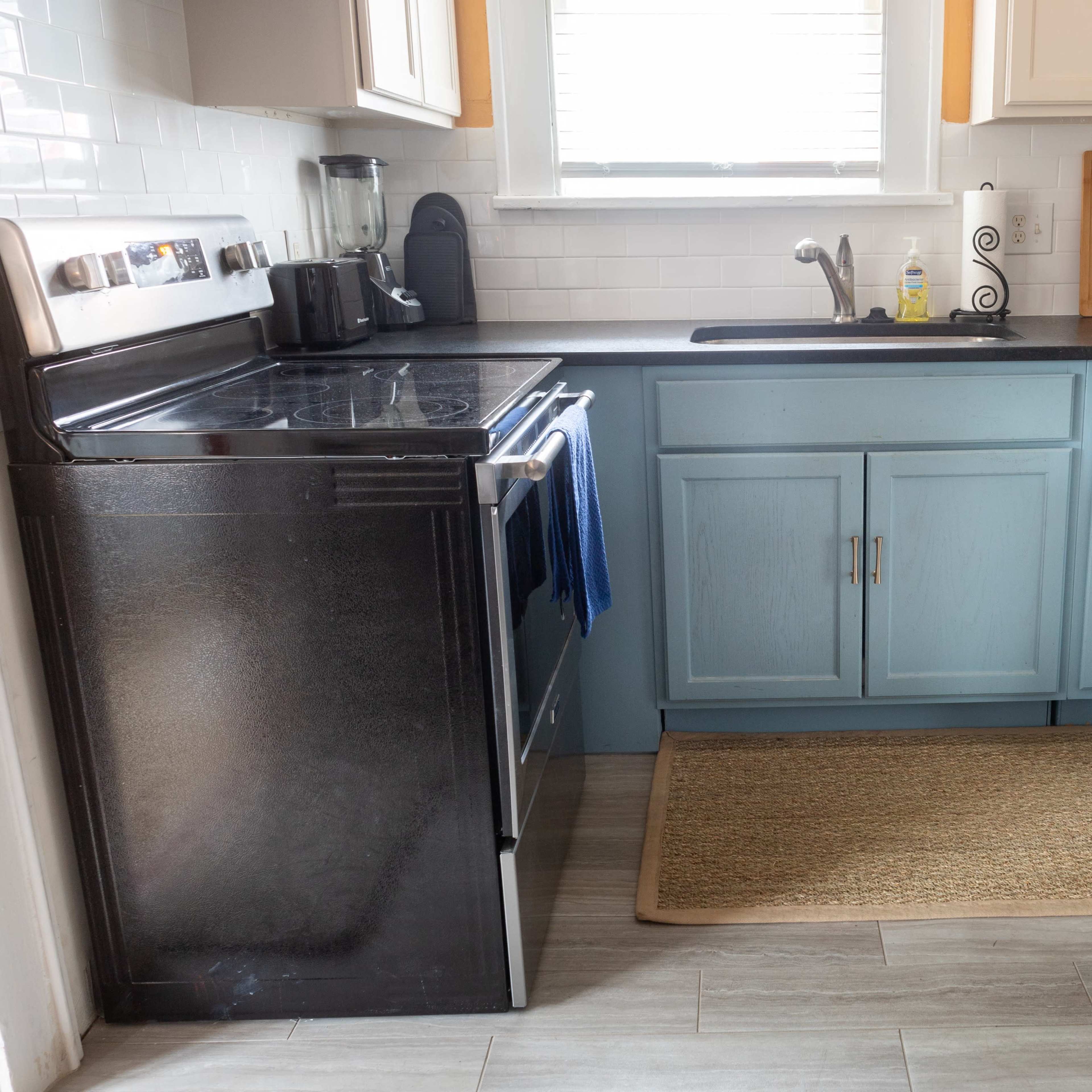 A kitchen corner featuring a black refrigerator, a blue cabinet, a stainless steel dishwasher, and a countertop with a sink.