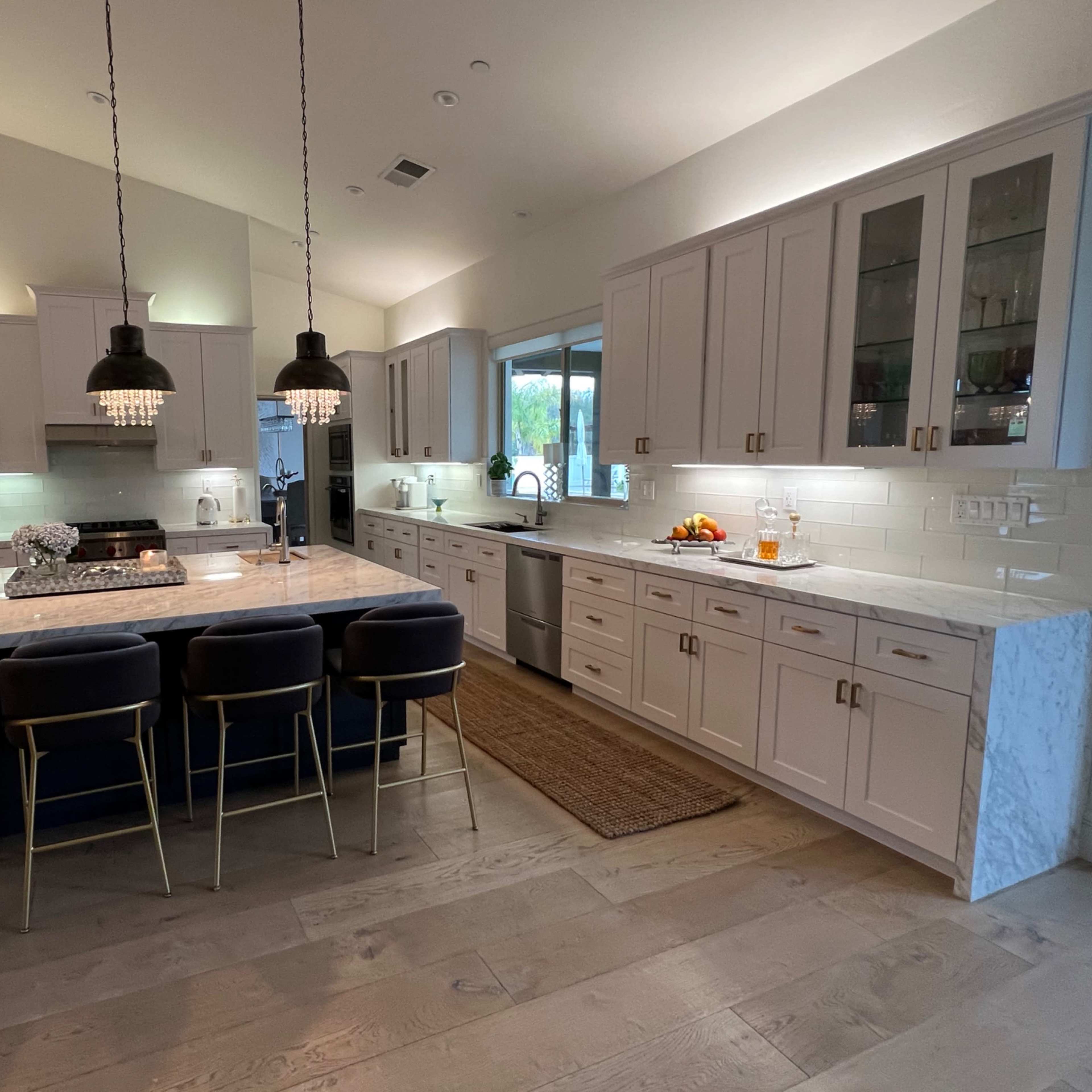 A modern kitchen featuring a large island with seating, pendant lights, white cabinetry, and stainless steel appliances.