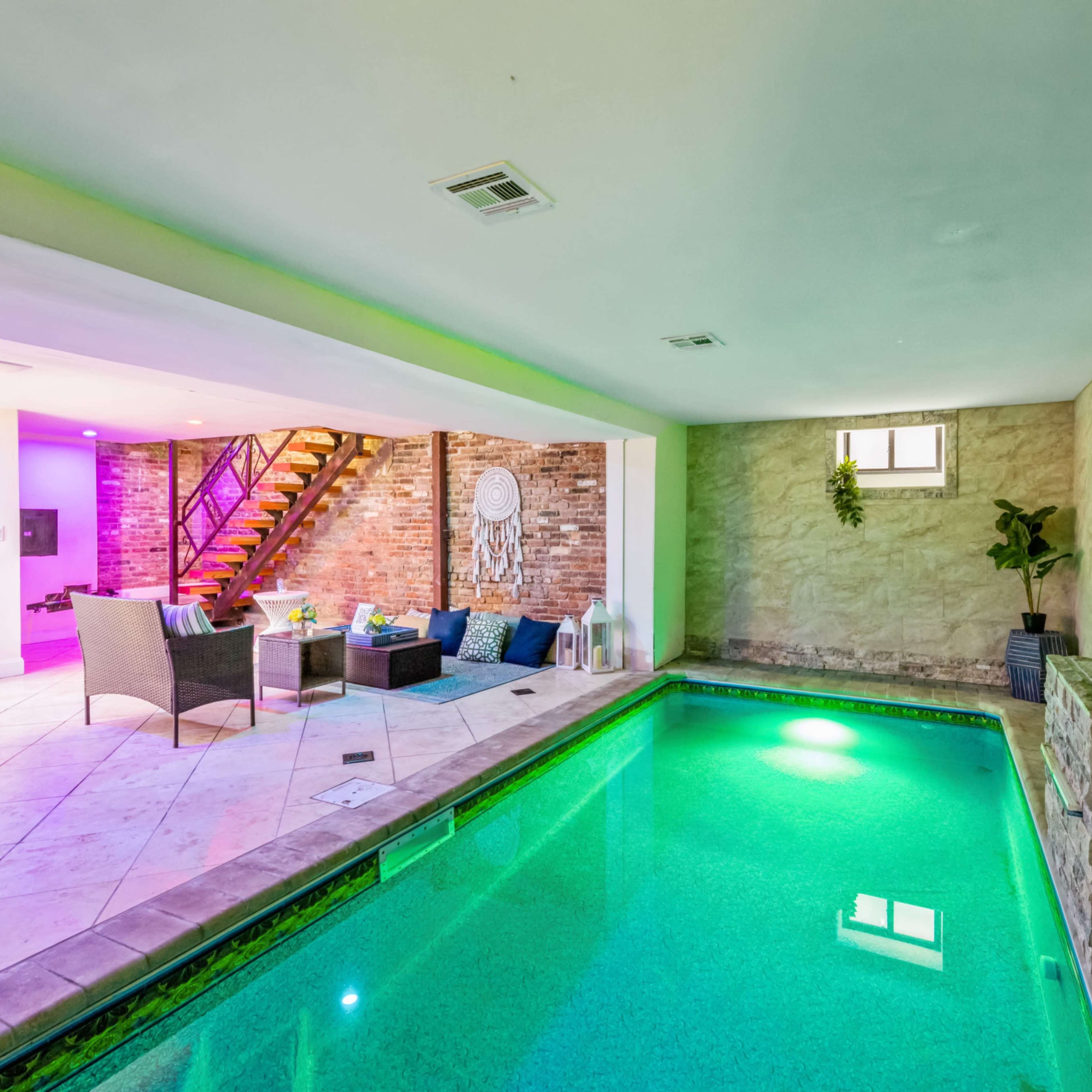 An indoor pool area with green water, adjacent to a seating area featuring colorful lighting and a staircase in the background.