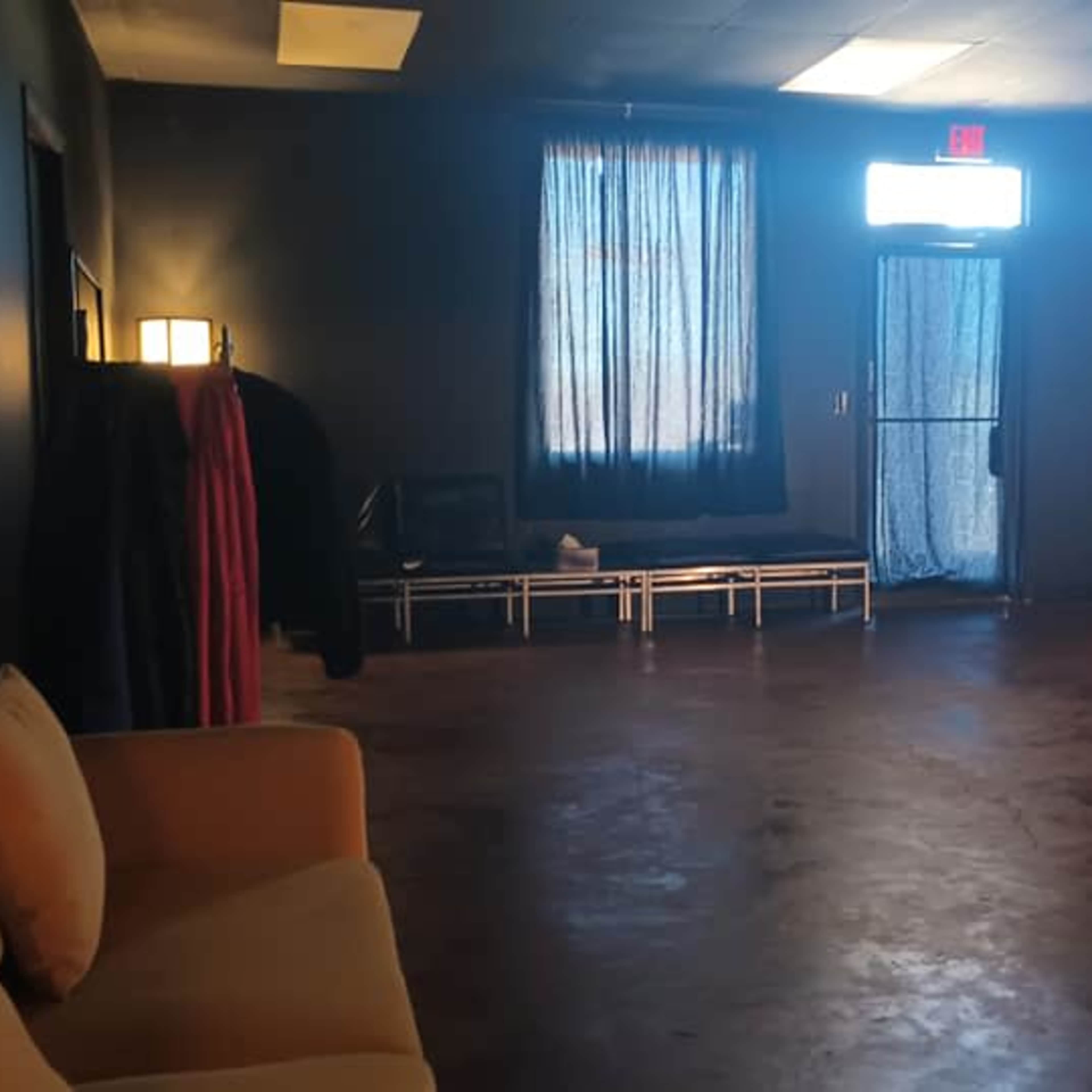 The room features a sofa, a table with a candle, and a door leading outside, all under dim lighting with a blue curtain.