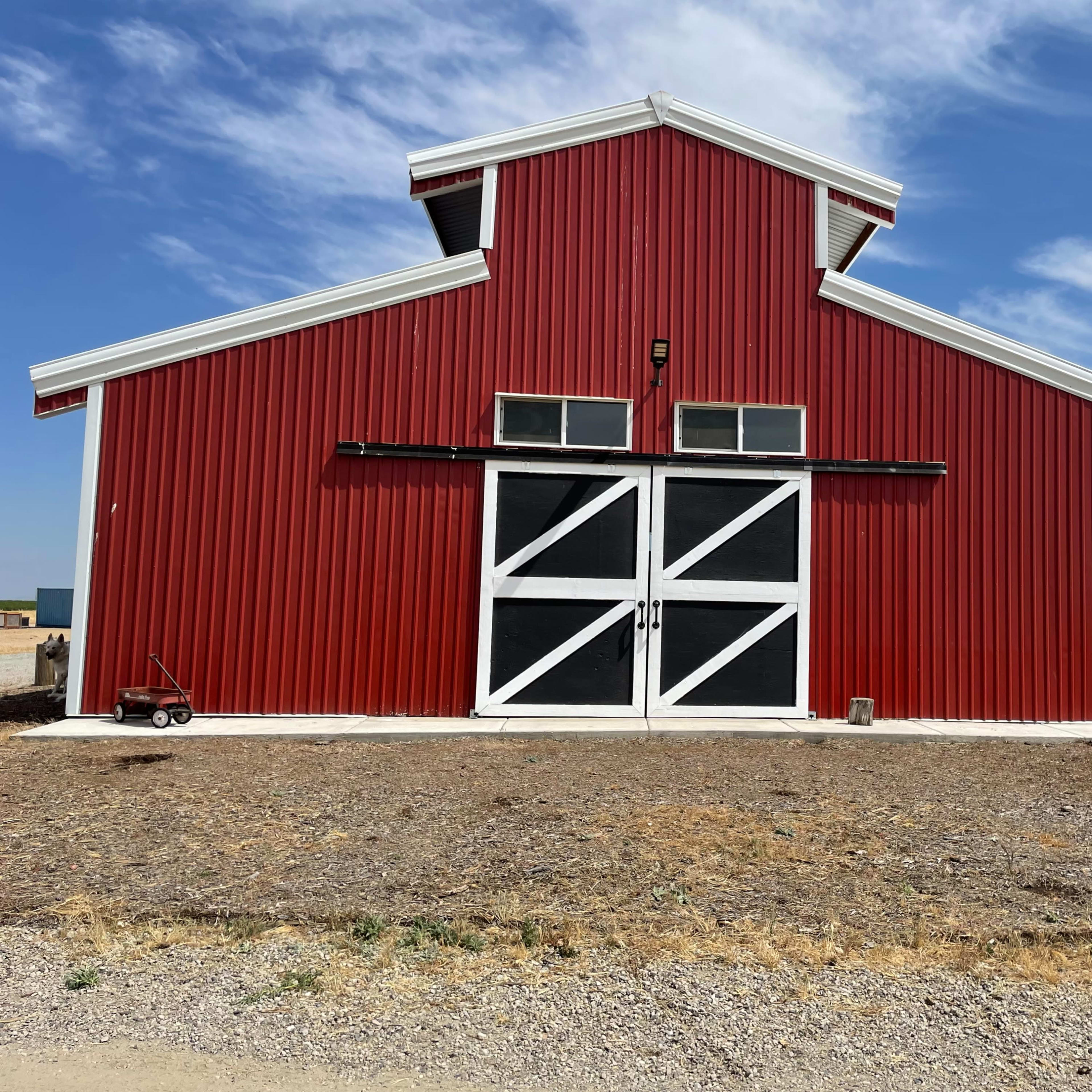 A large red barn with a white door structure, situated in a dry, open landscape.