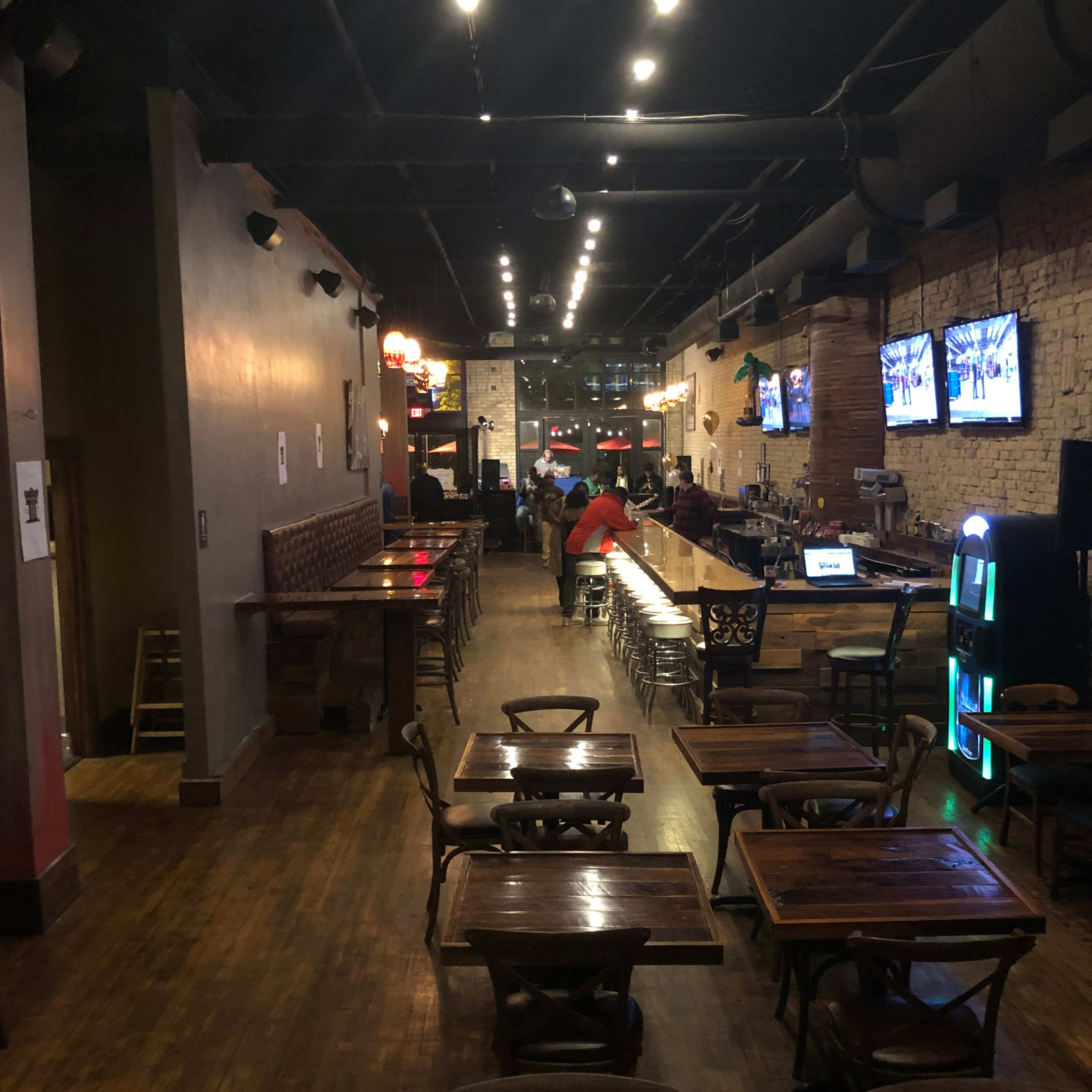 An interior view of a bar or pub with wooden tables, a long counter, and several televisions mounted on the walls.