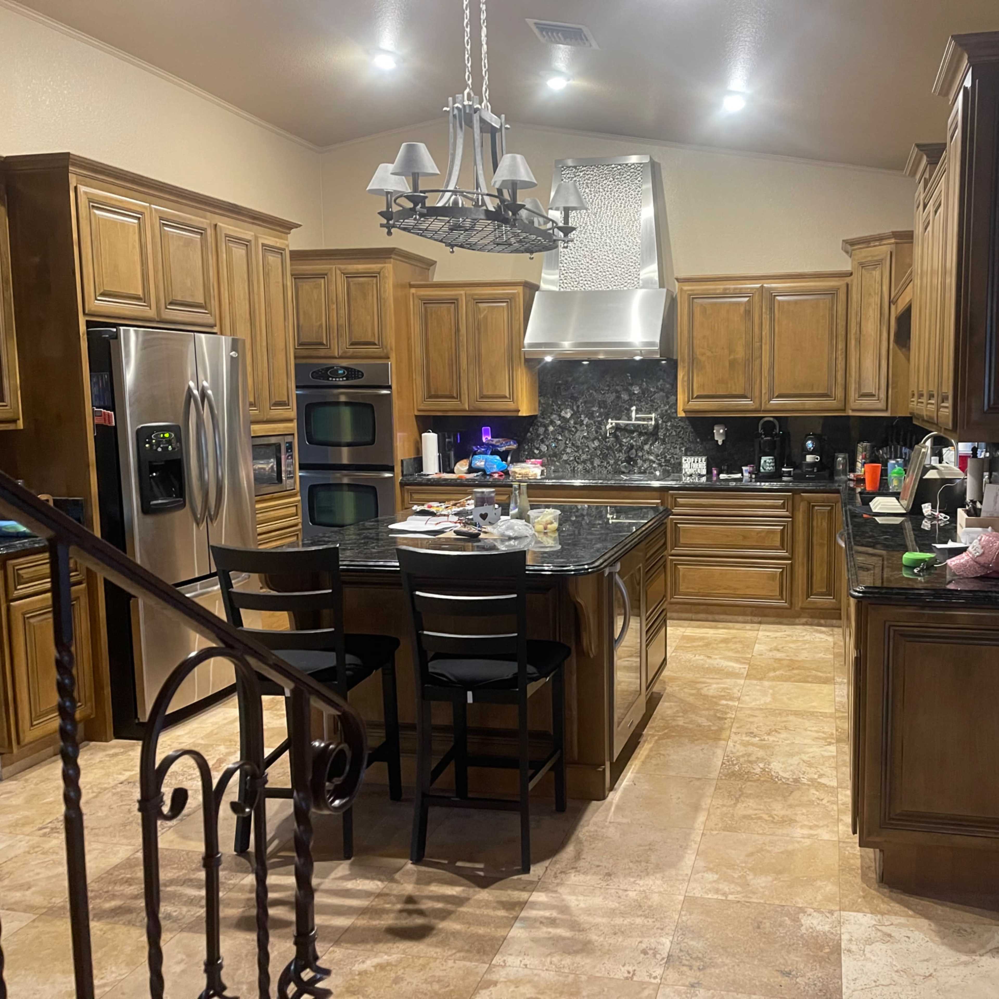 A spacious kitchen featuring wooden cabinetry, a large island with stools, and various appliances, set in a well-lit area with tile flooring.