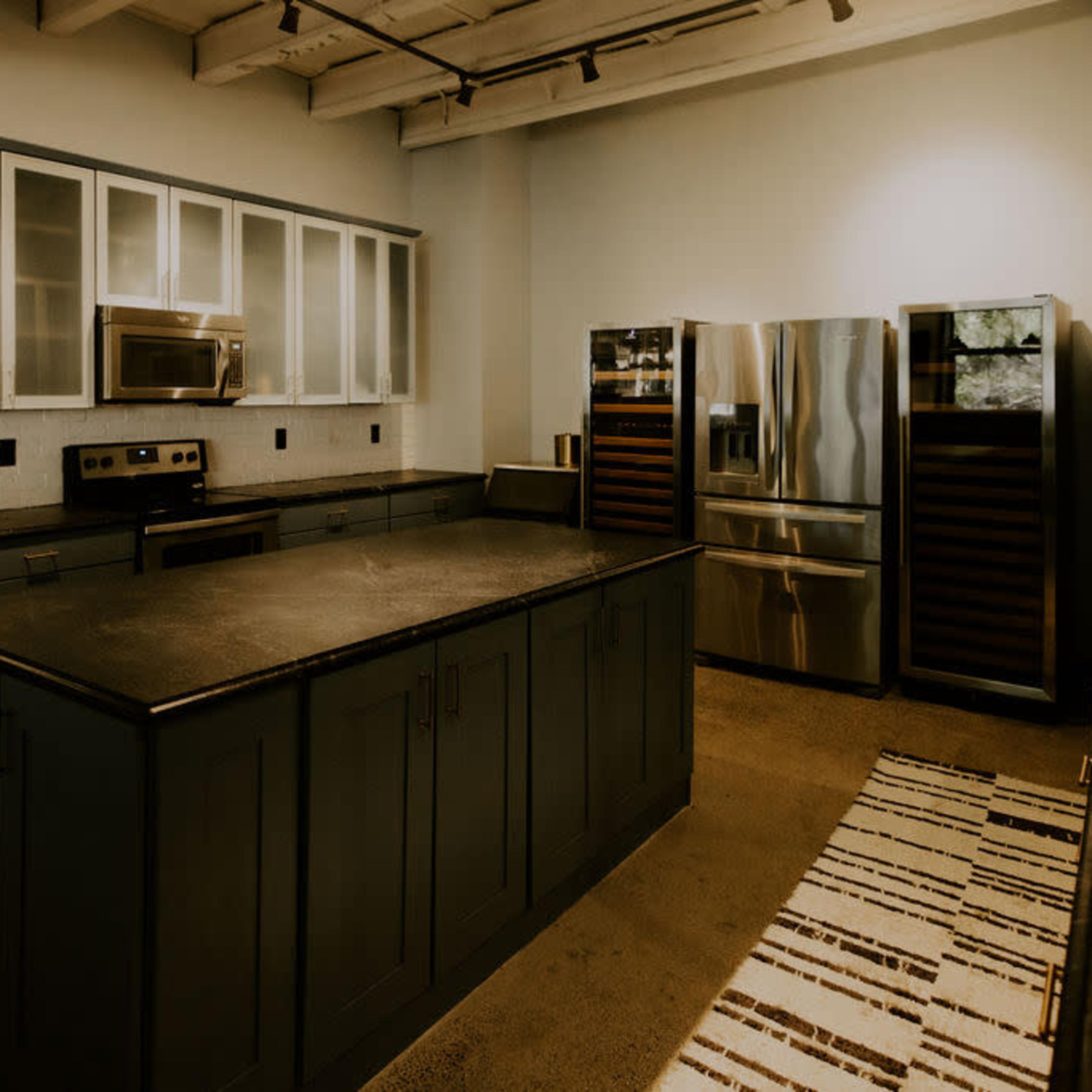 A modern kitchen with a central island, dark cabinetry, stainless steel appliances, and a patterned rug on the floor.