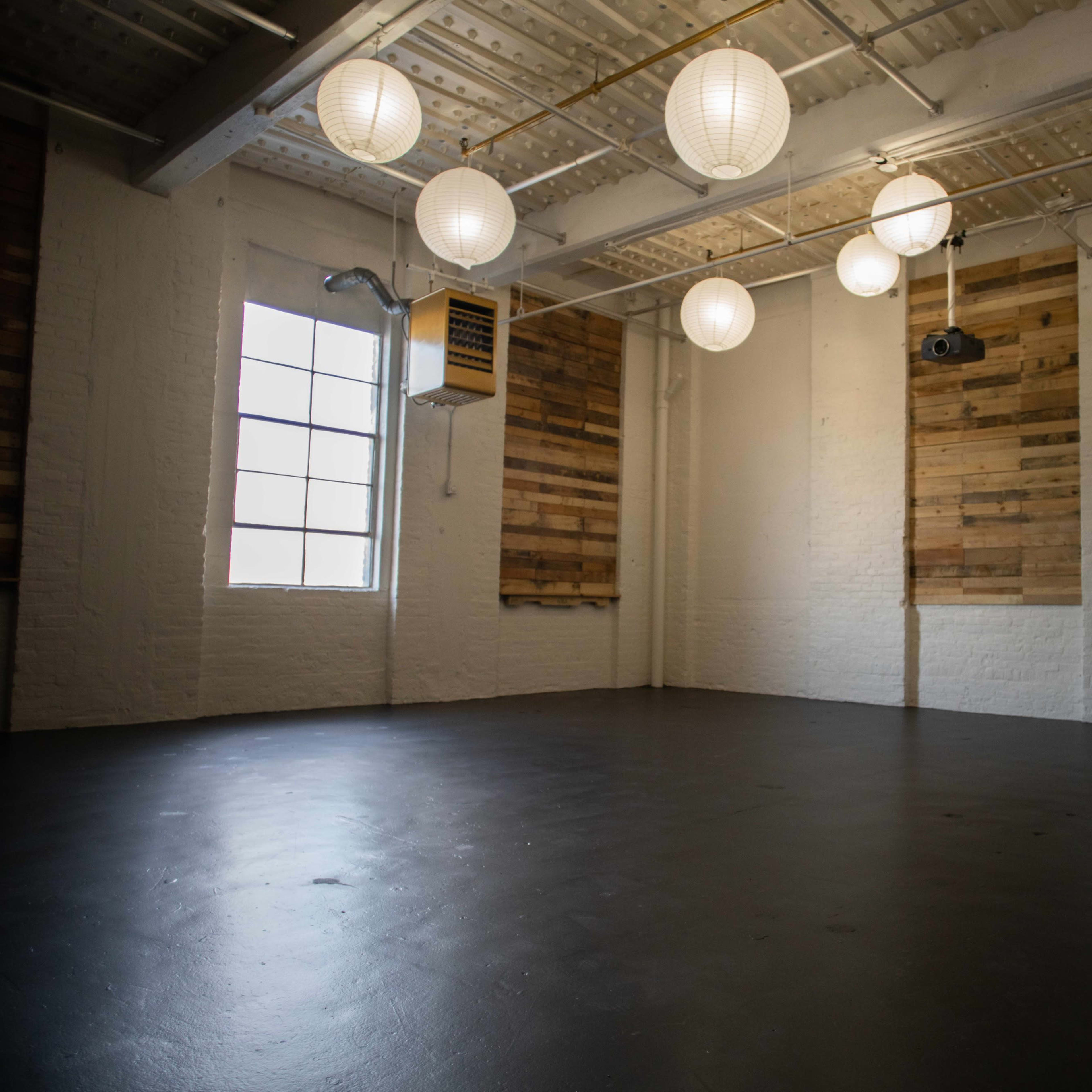 An empty room with a polished black floor, adorned with round paper lanterns hanging from the ceiling and wooden wall panels on two sides.