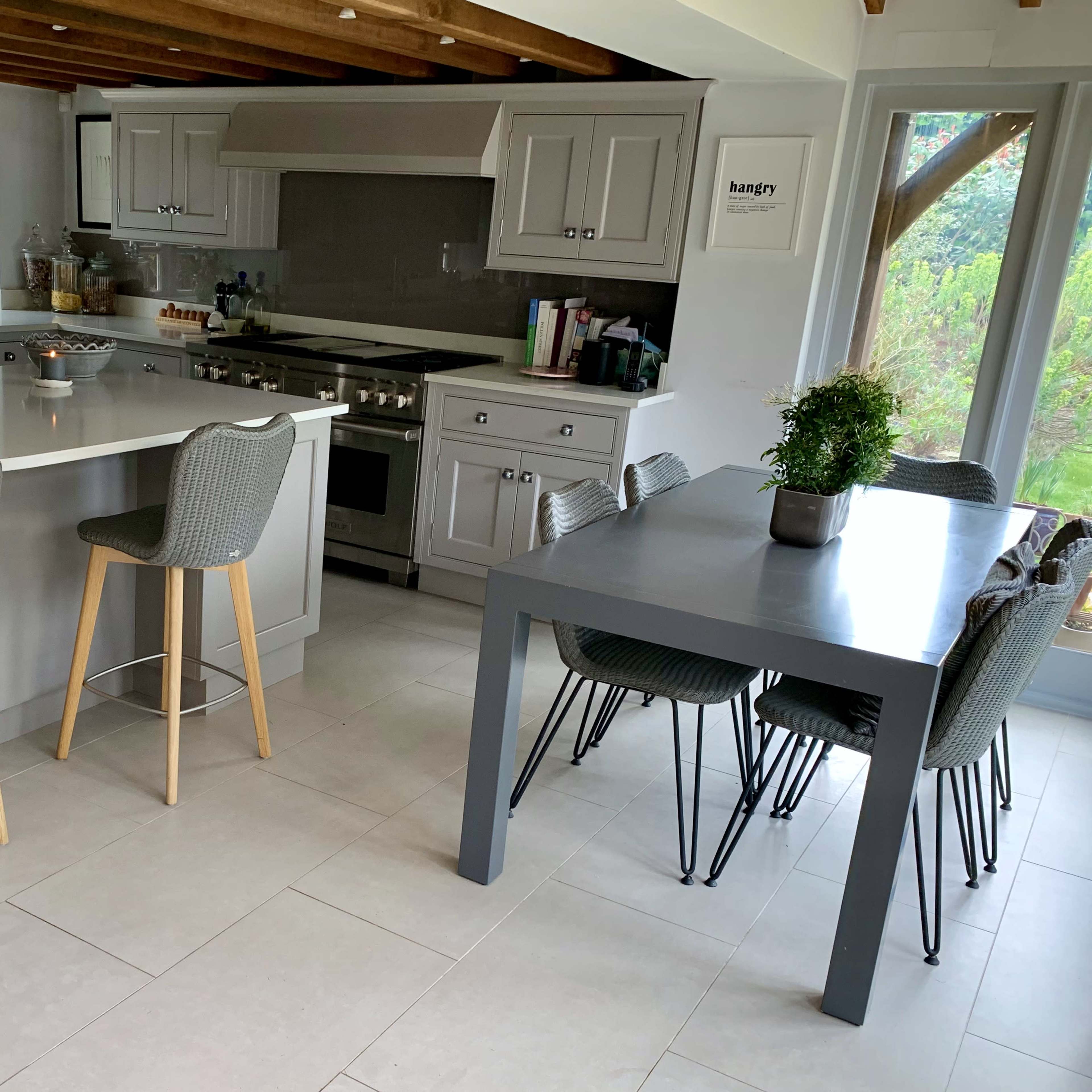 A modern kitchen features a central island with barstools, a dining table, and large windows that let in natural light.