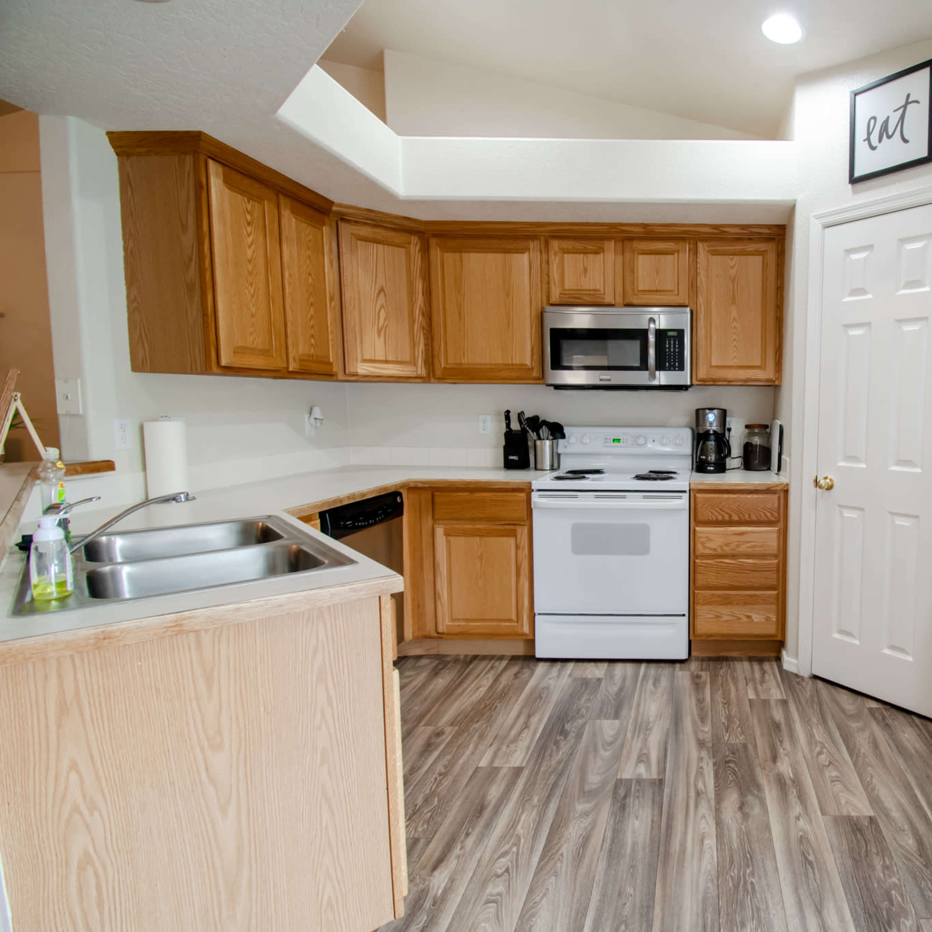 A compact kitchen with wooden cabinets, white appliances, and a light-colored countertop.